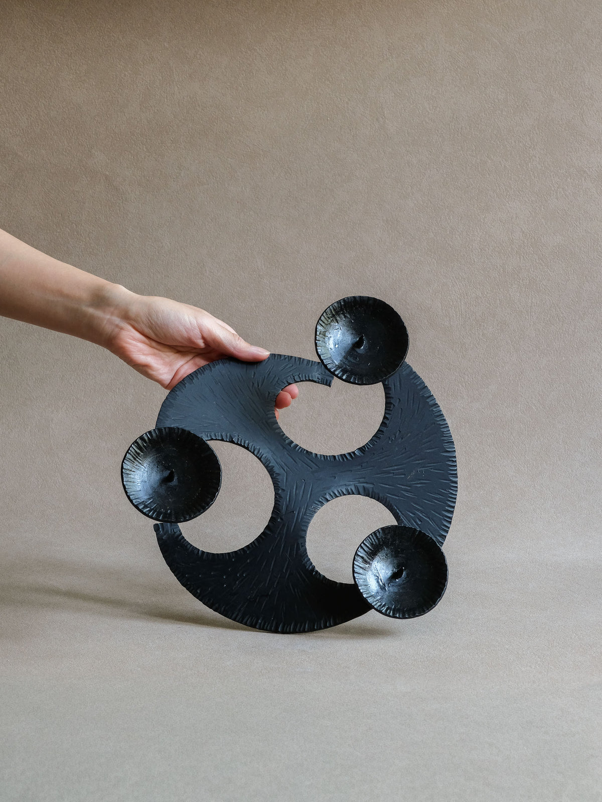 Large three-arm cast iron candleholder held upright to show scale, curved form and three dishes.