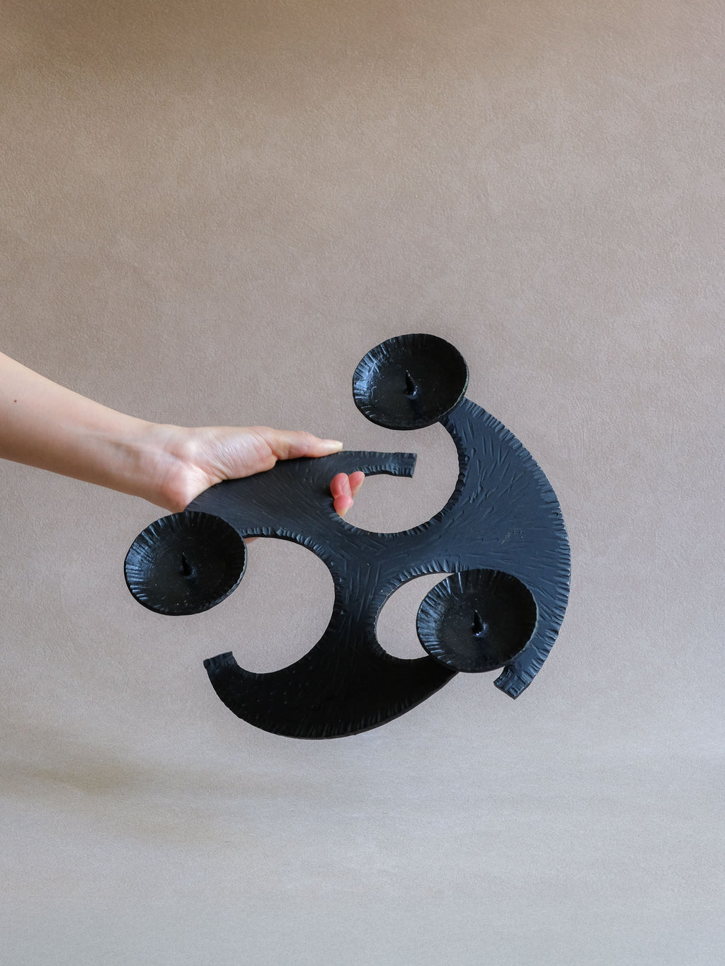 Top view of the large Brutalist candleholder held by hand, showing scale and three-arm construction.