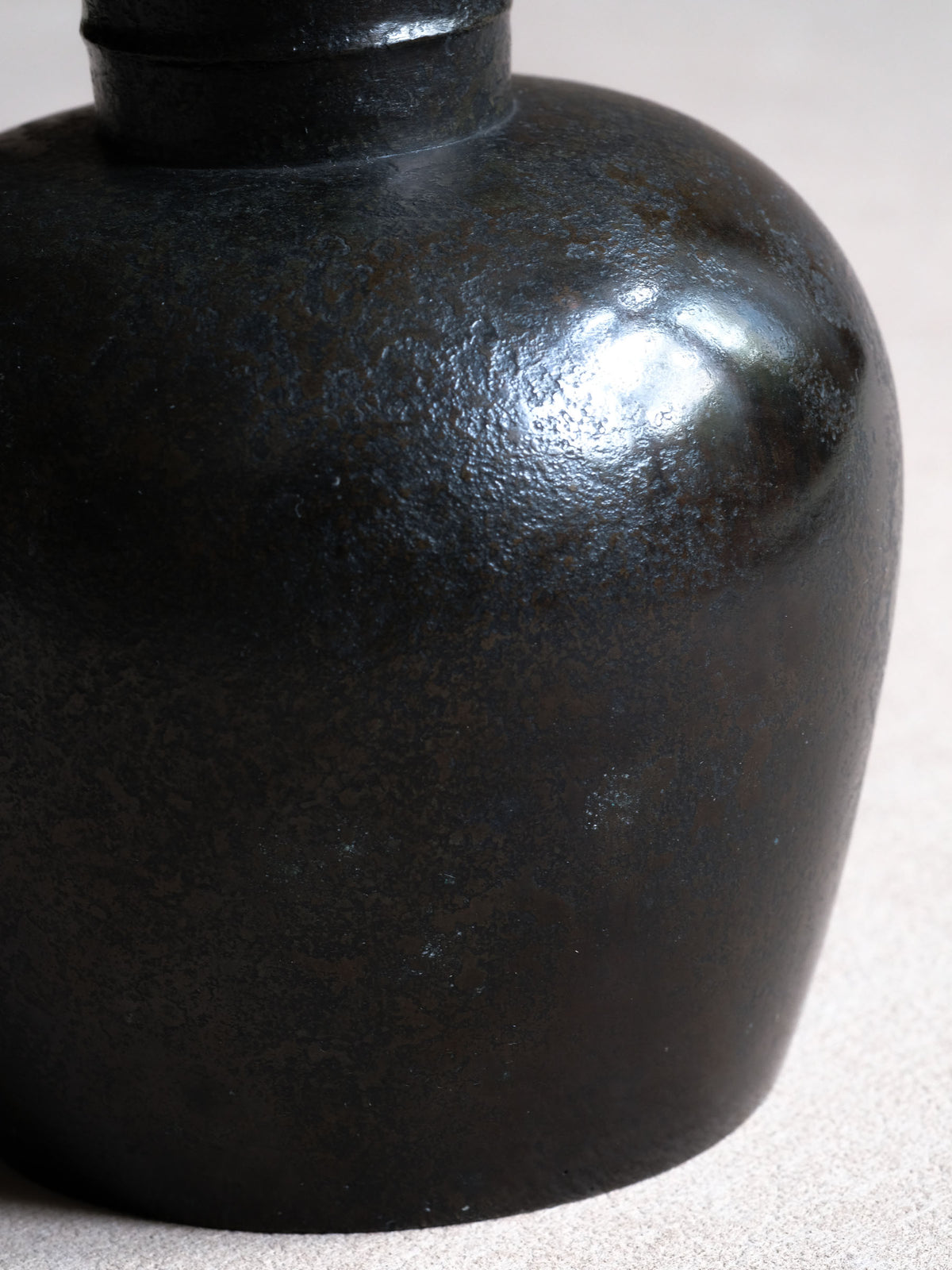 Close-up of Maruyama Fubo cast copper vase surface, showing dark metallic tone and small pale surface marks.