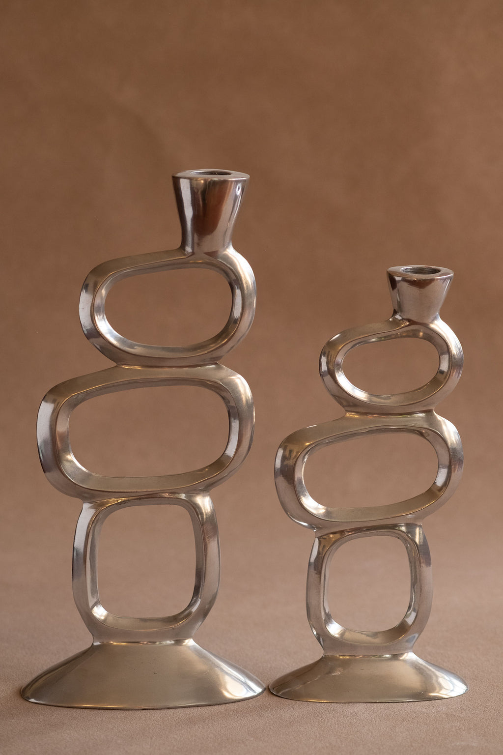 Pair of polished aluminium Matthew Hilton Circle candle holders shown front-facing, with open geometric ring forms and wide bases.
