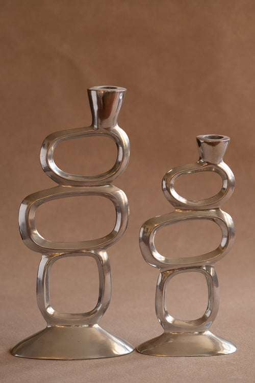 Pair of polished aluminium Matthew Hilton Circle candle holders shown front-facing, with open geometric ring forms and wide bases.
