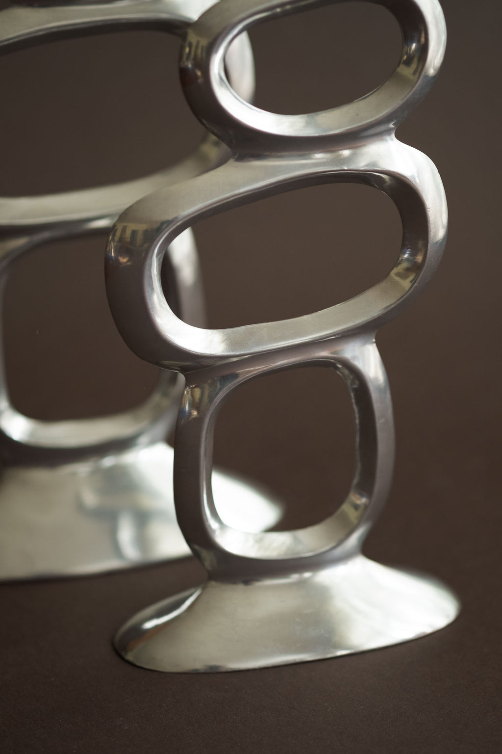 Close-up of the polished aluminium ring openings and base detail on the Matthew Hilton Circle candle holders.
