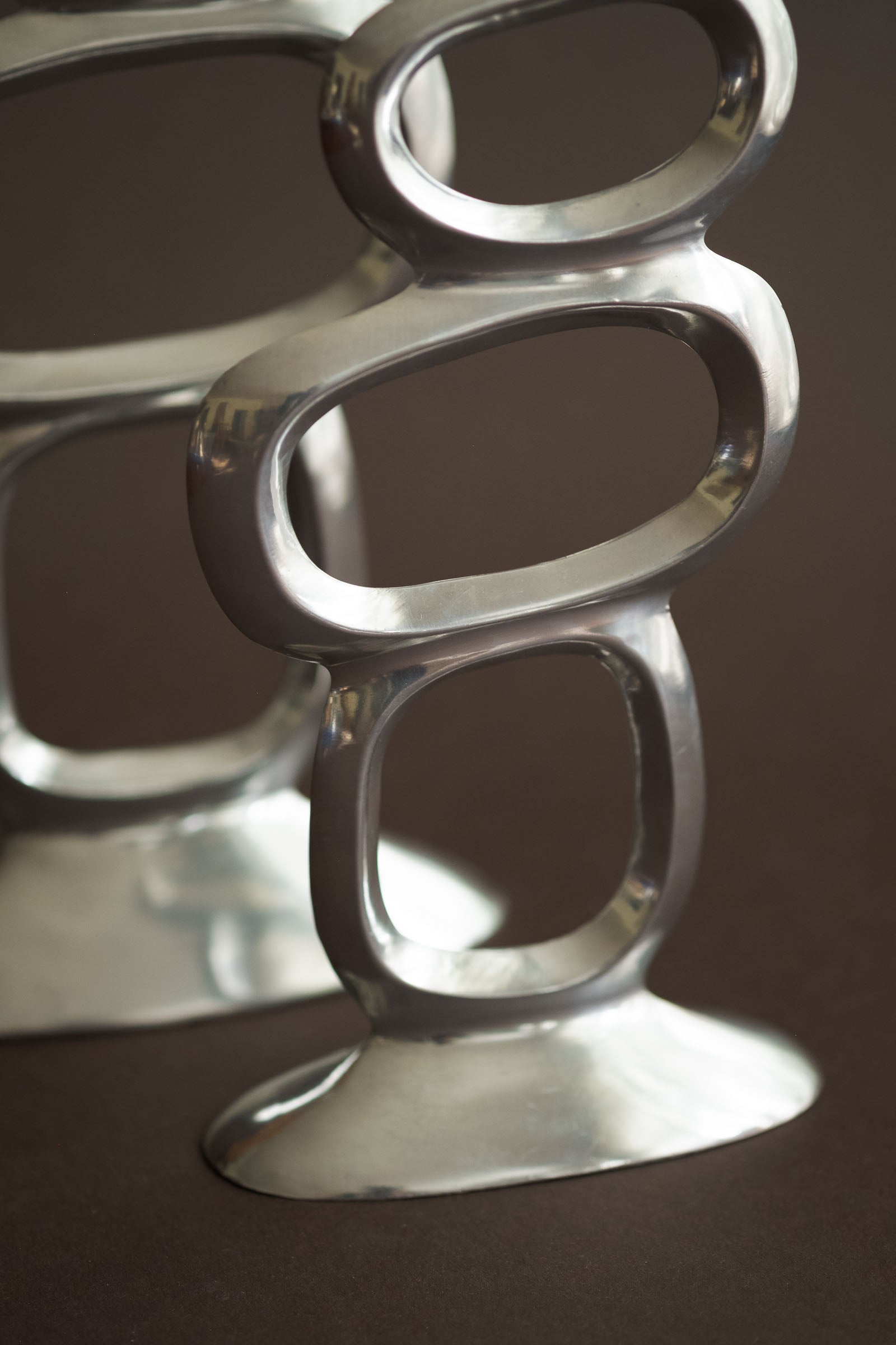 Close-up of the polished aluminium ring openings and base detail on the Matthew Hilton Circle candle holders.
