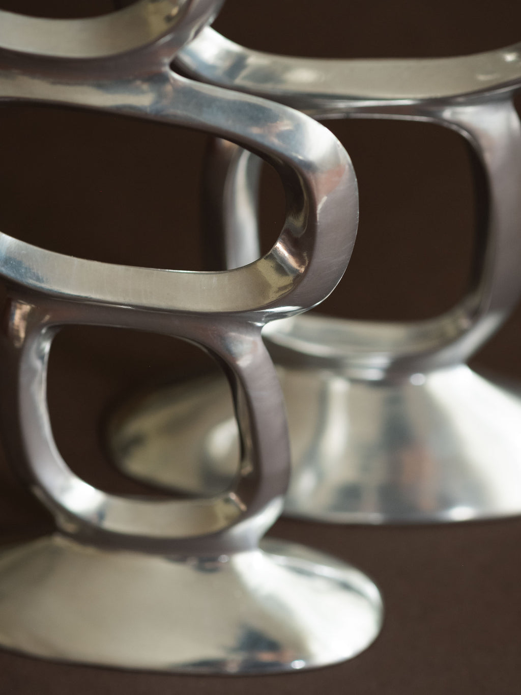 Close-up of the polished aluminium surface and rounded open ring form on the Matthew Hilton Circle candle holders.
