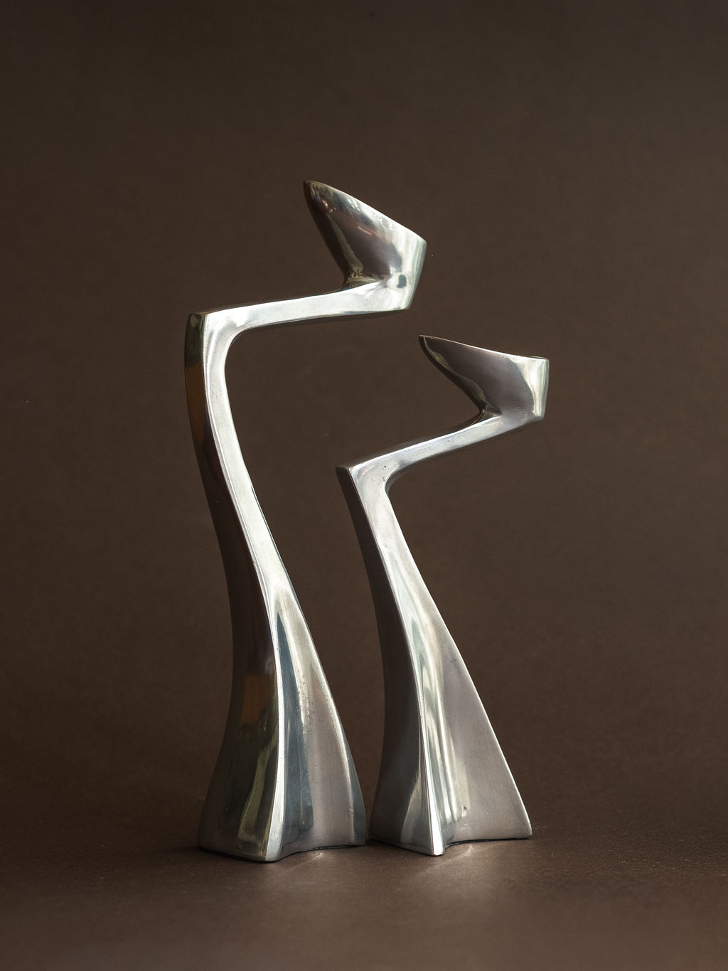 Pair of polished aluminium Swan candle holders in a close front view, showing the tall curved forms and sculptural bases.
