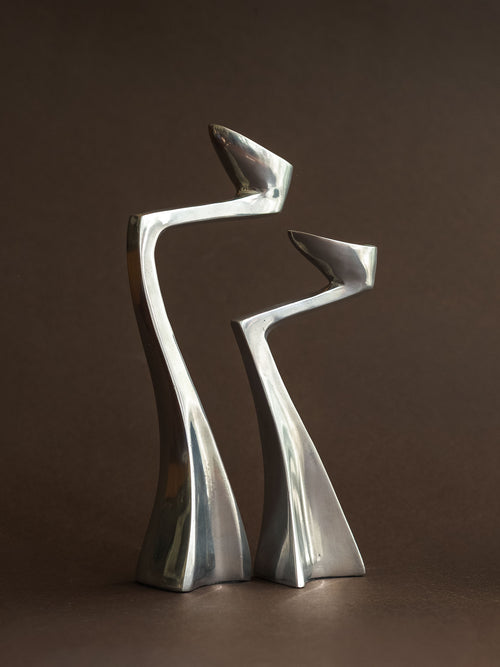 Pair of polished aluminium Swan candle holders in a close front view, showing the tall curved forms and sculptural bases.
