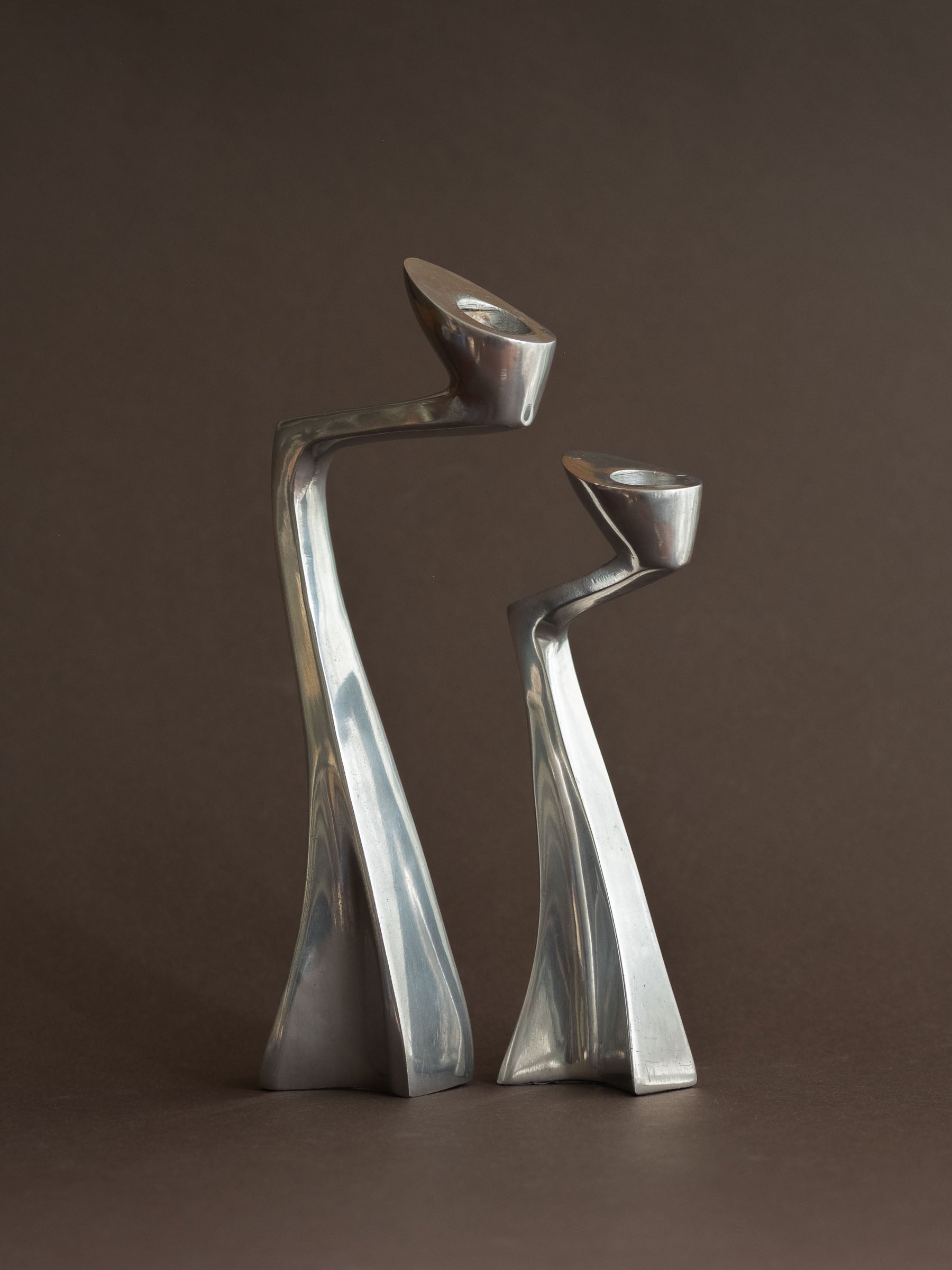 Pair of polished aluminium Swan candle holders shown from an angled front view, with the candle openings visible at the top.
