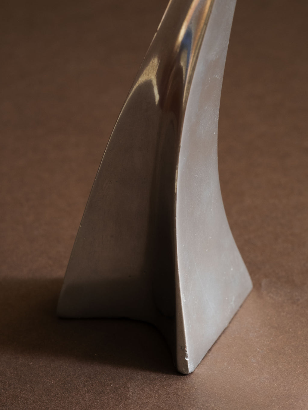 Close-up of the base of a polished aluminium Swan candle holder, showing the curved foot and reflective surface.
