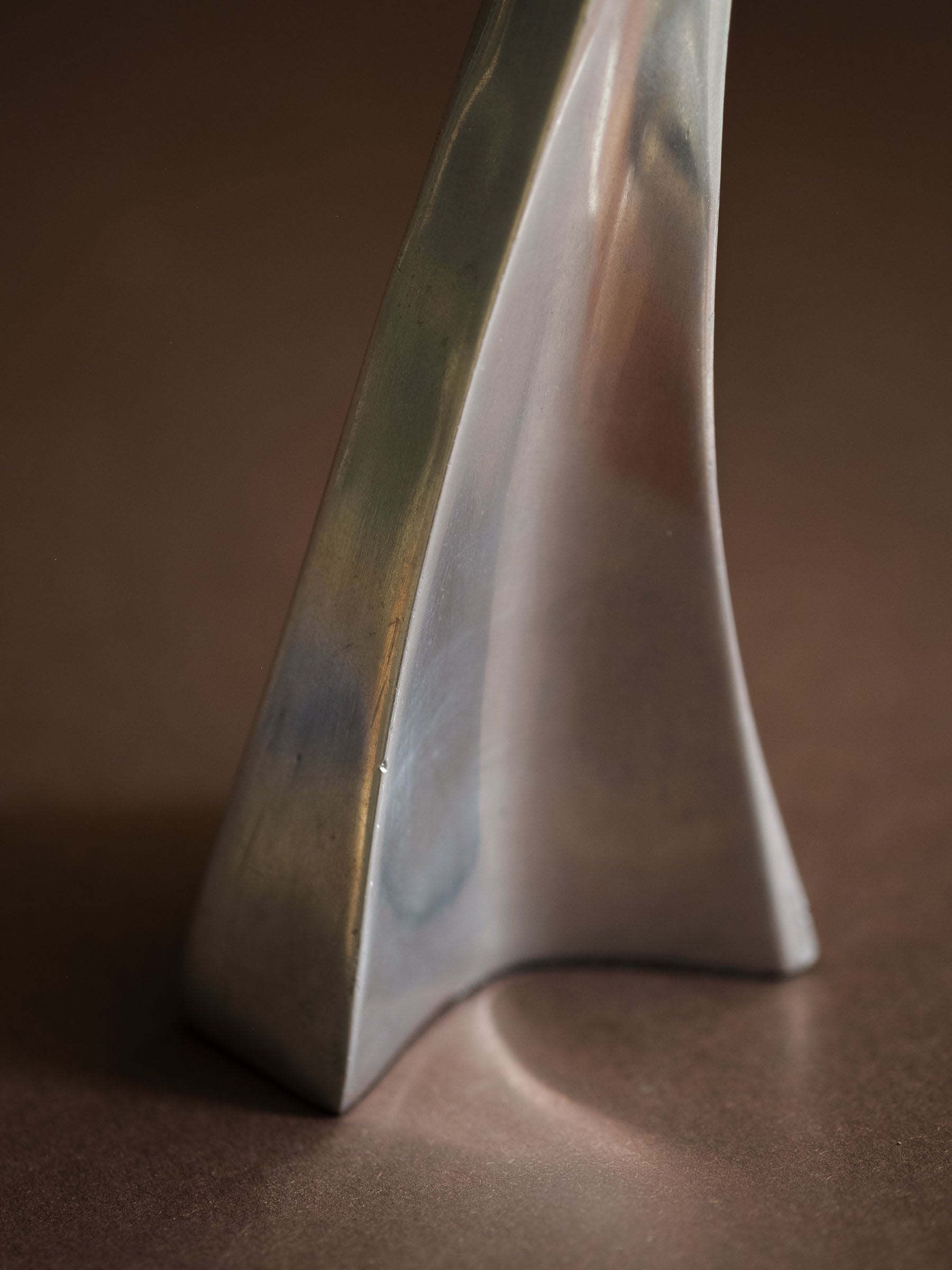 Close-up of the polished aluminium surface and base form of a Swan candle holder, showing light scratches and natural vintage wear.
