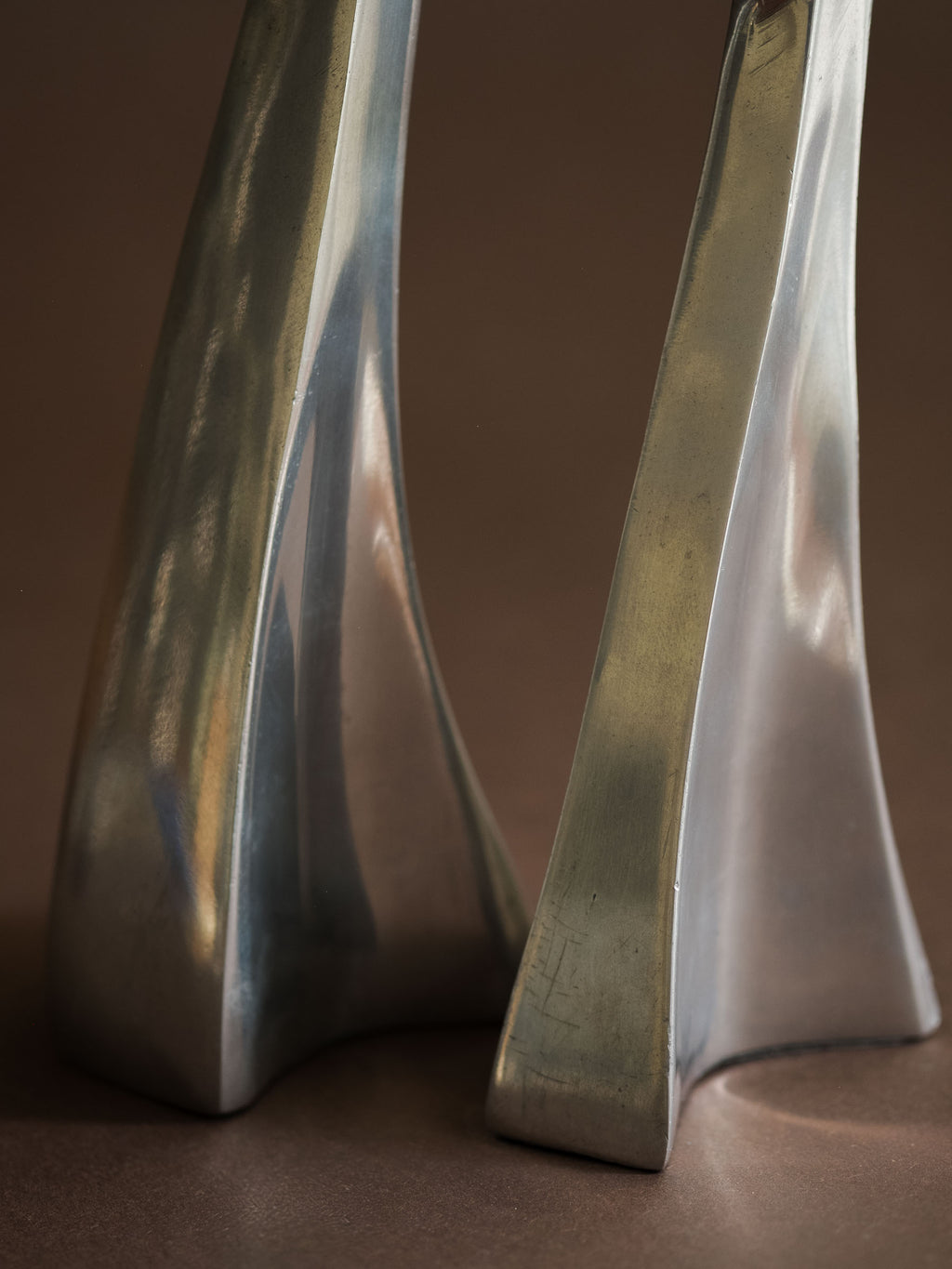 Close-up of the lower sections of the polished aluminium Swan candle holders, showing sculptural bases and surface patina.