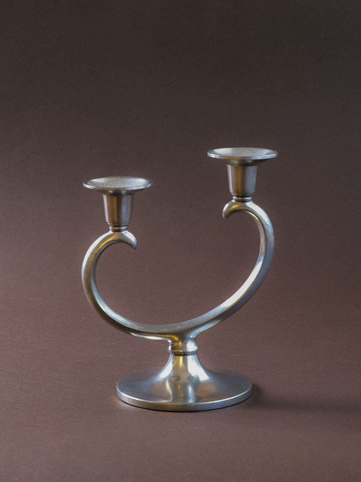 Metawa two-arm pewter candleholder, front view showing the sweeping asymmetric arms and round base.