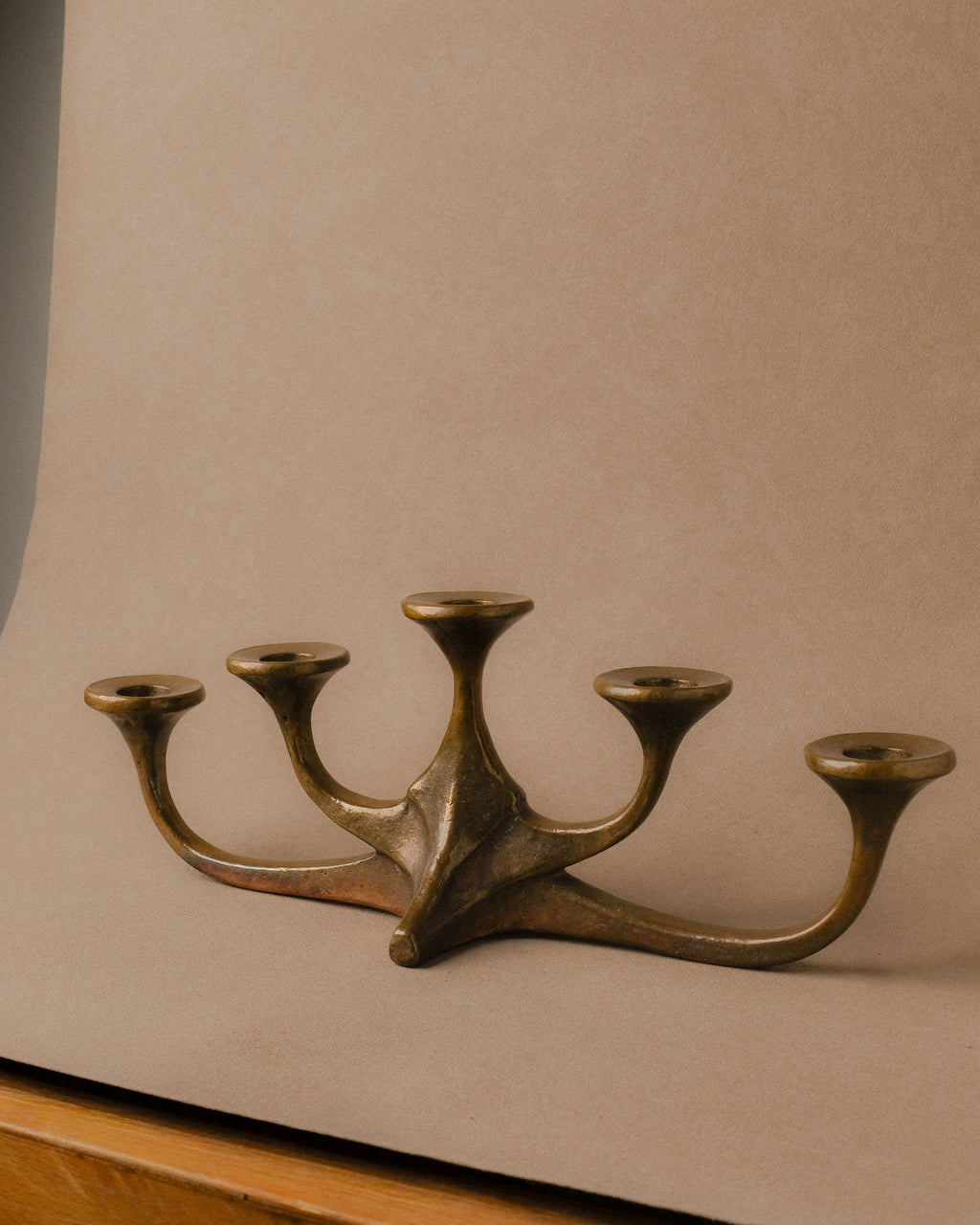 Angled view of mid-century bronze candleholder with five arms, Germany, 1960s–70s, photographed on a wooden table with a beige backdrop.