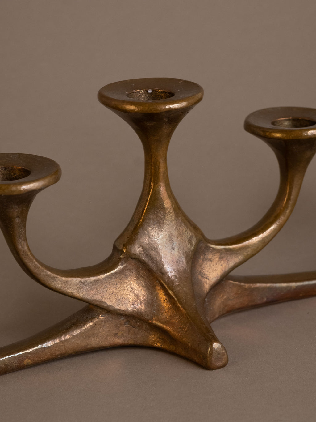 Close-up of central base of cast bronze candleholder showing sculptural form and patina.