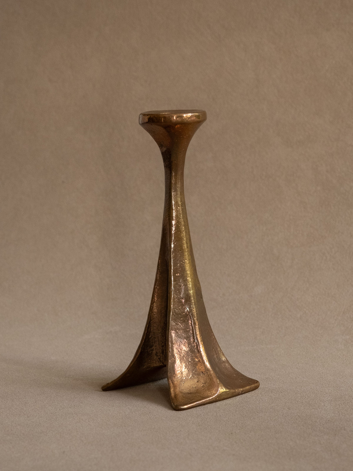 Angled view of the Michael Harjes bronze candleholder showing its slender stem and three flared feet.