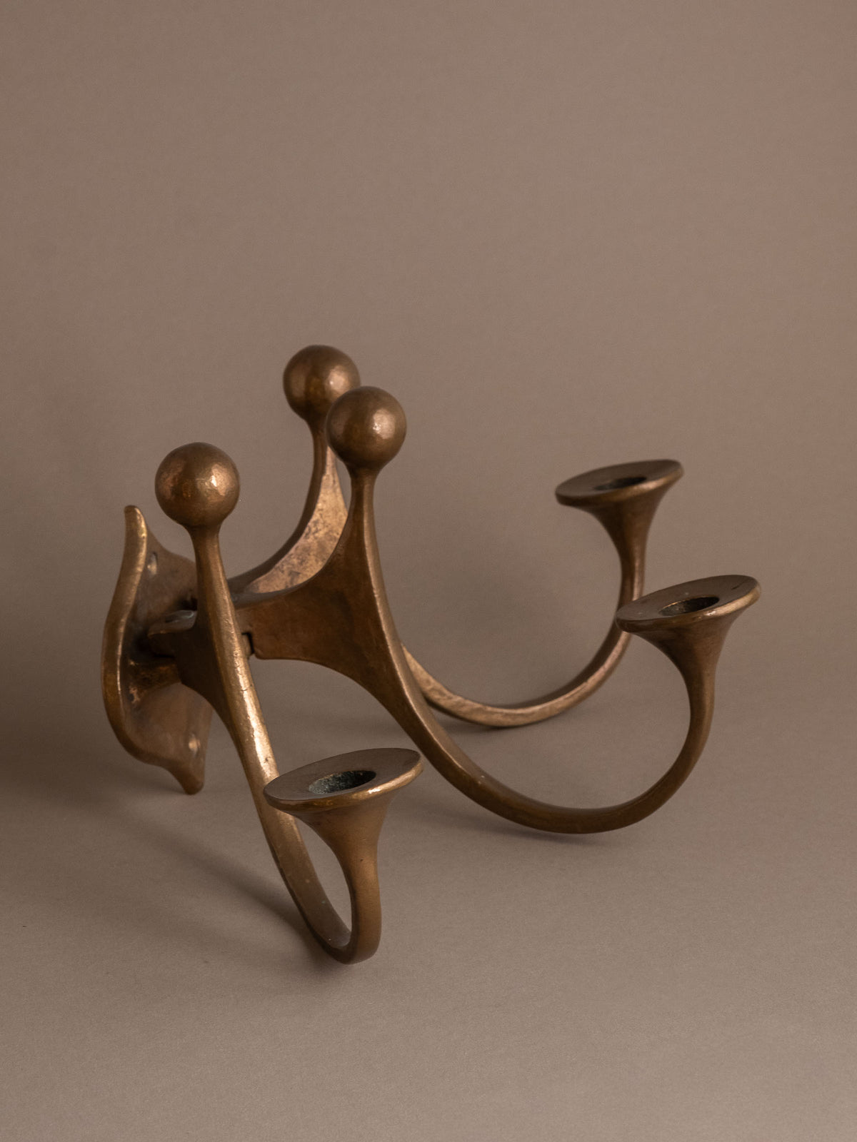 Angled side view of the Michael Harjes bronze wall candleholder showing its sweeping arms and aged bronze surface.