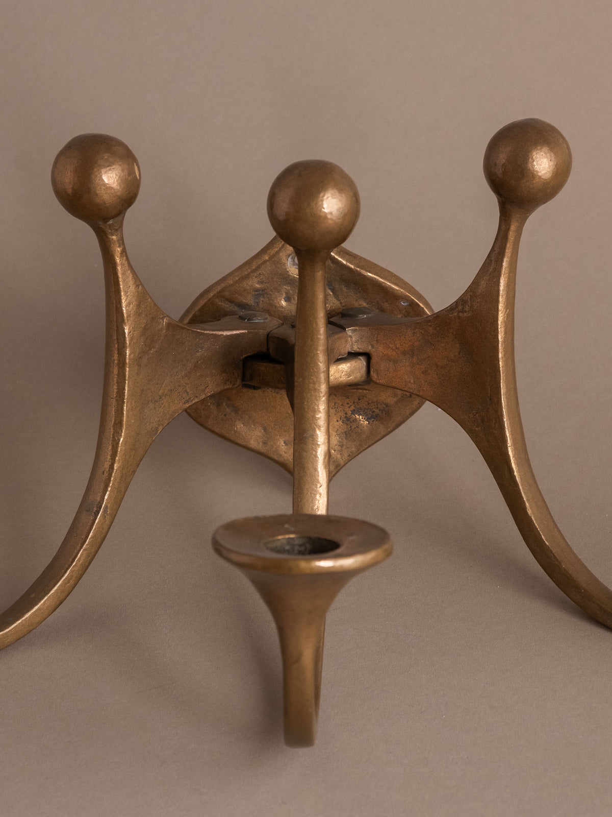 Close view of the central candle cup, ball finials and articulated bronze arms.