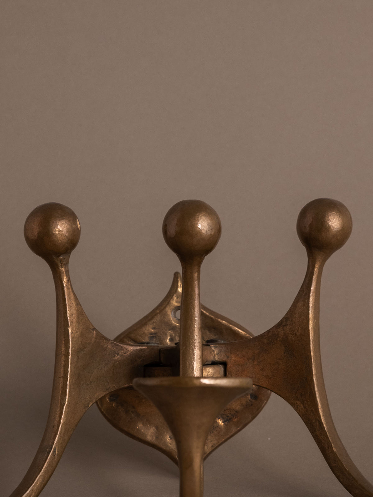 Rear mounting detail of the three-arm bronze wall candleholder showing the wall plate and jointed construction.