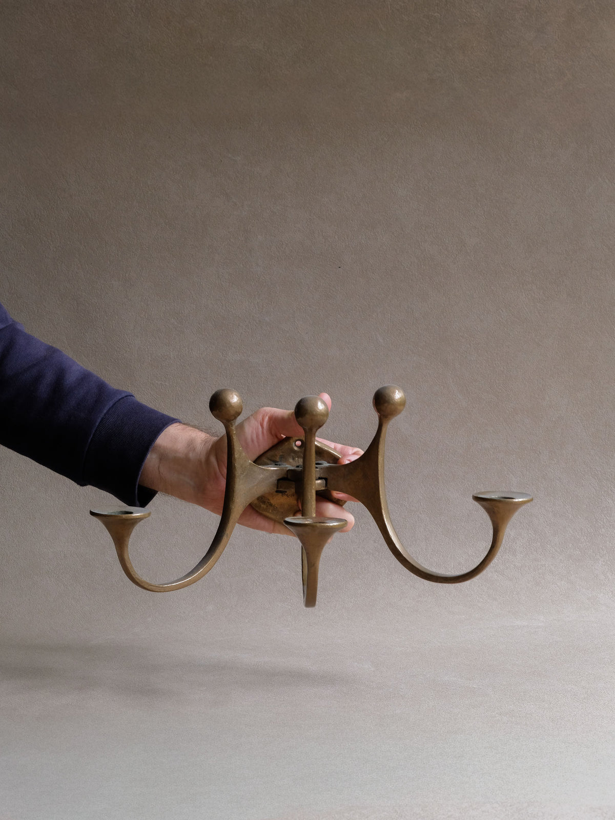 Hand-held scale view of the Michael Harjes bronze wall candleholder showing its broad projecting form.