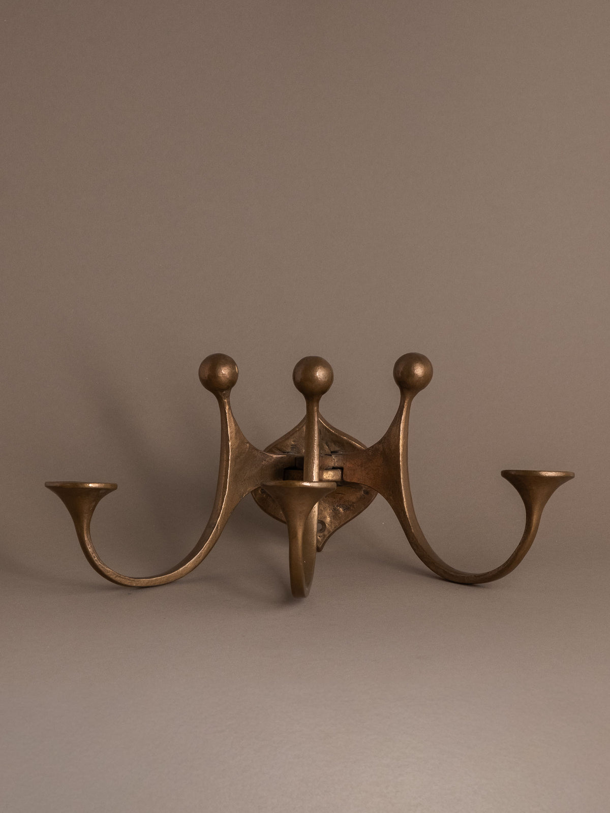 Three-quarter front view of a Michael Harjes three-arm bronze wall candleholder, Germany, c. 1960s.