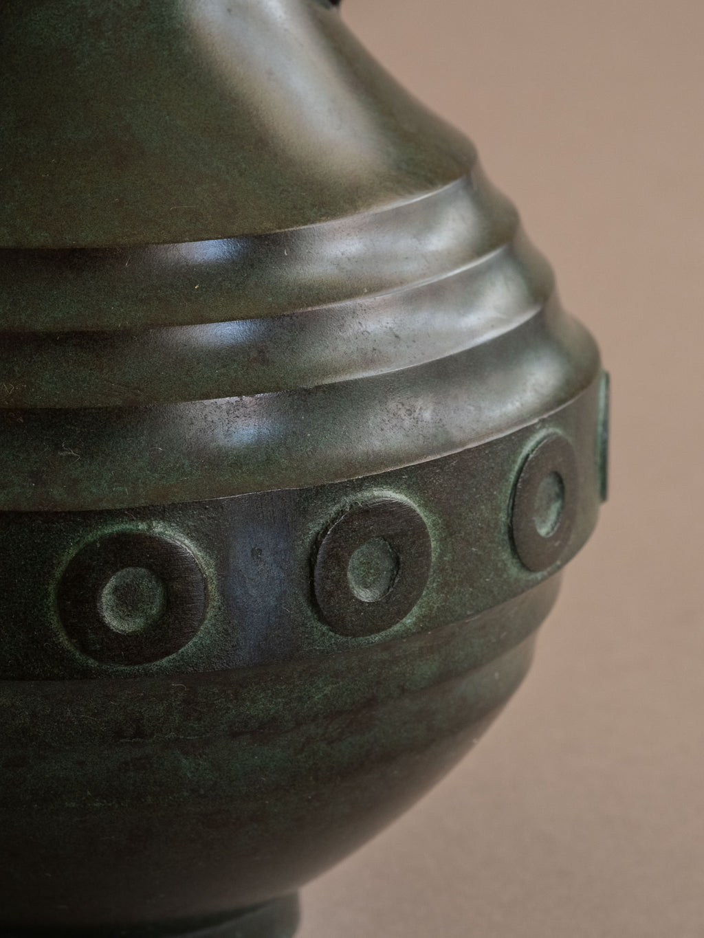 Close-up of janome circular relief band and dark green patinated bronze surface.