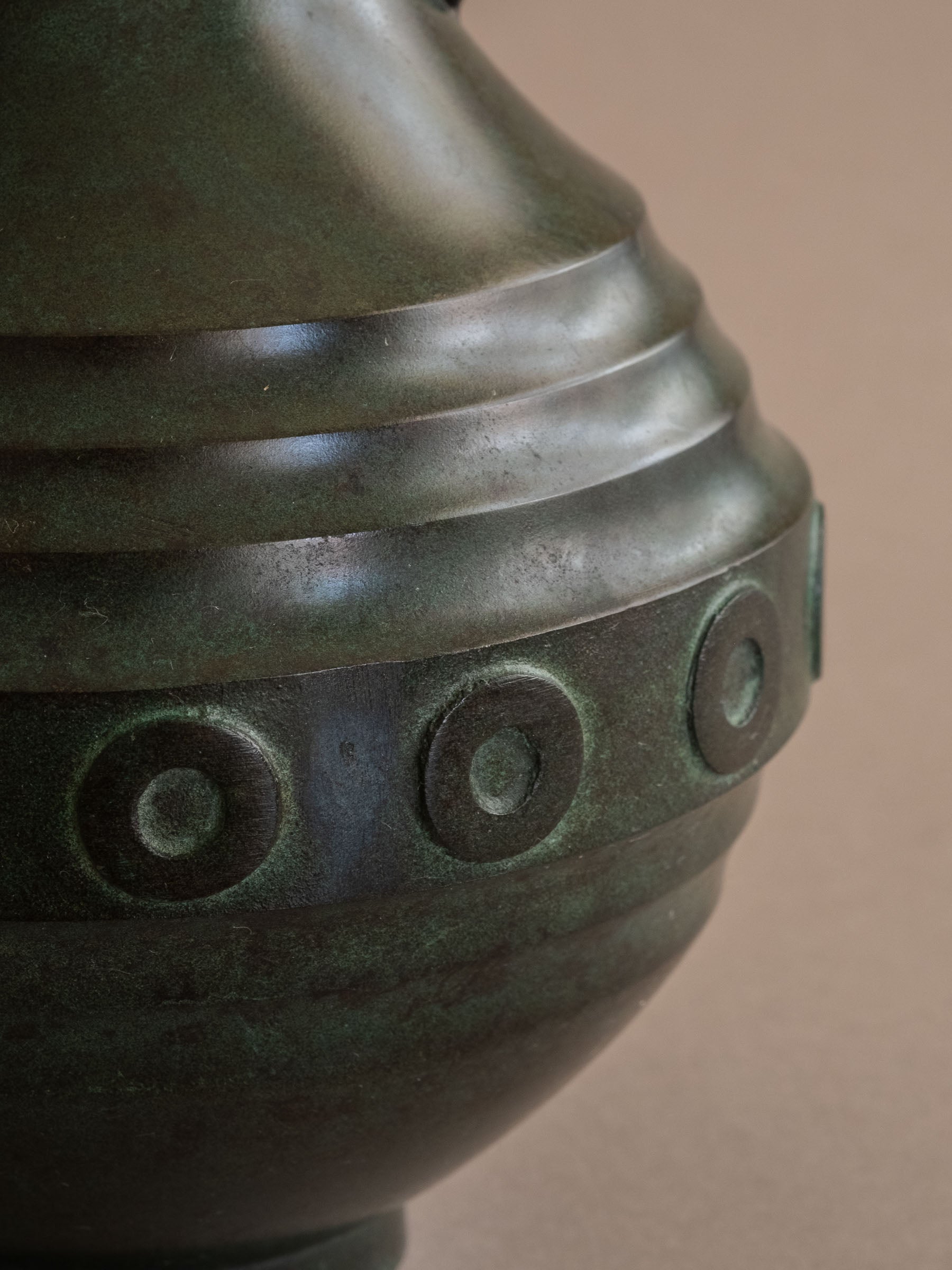 Close-up of janome circular relief band and dark green patinated bronze surface.