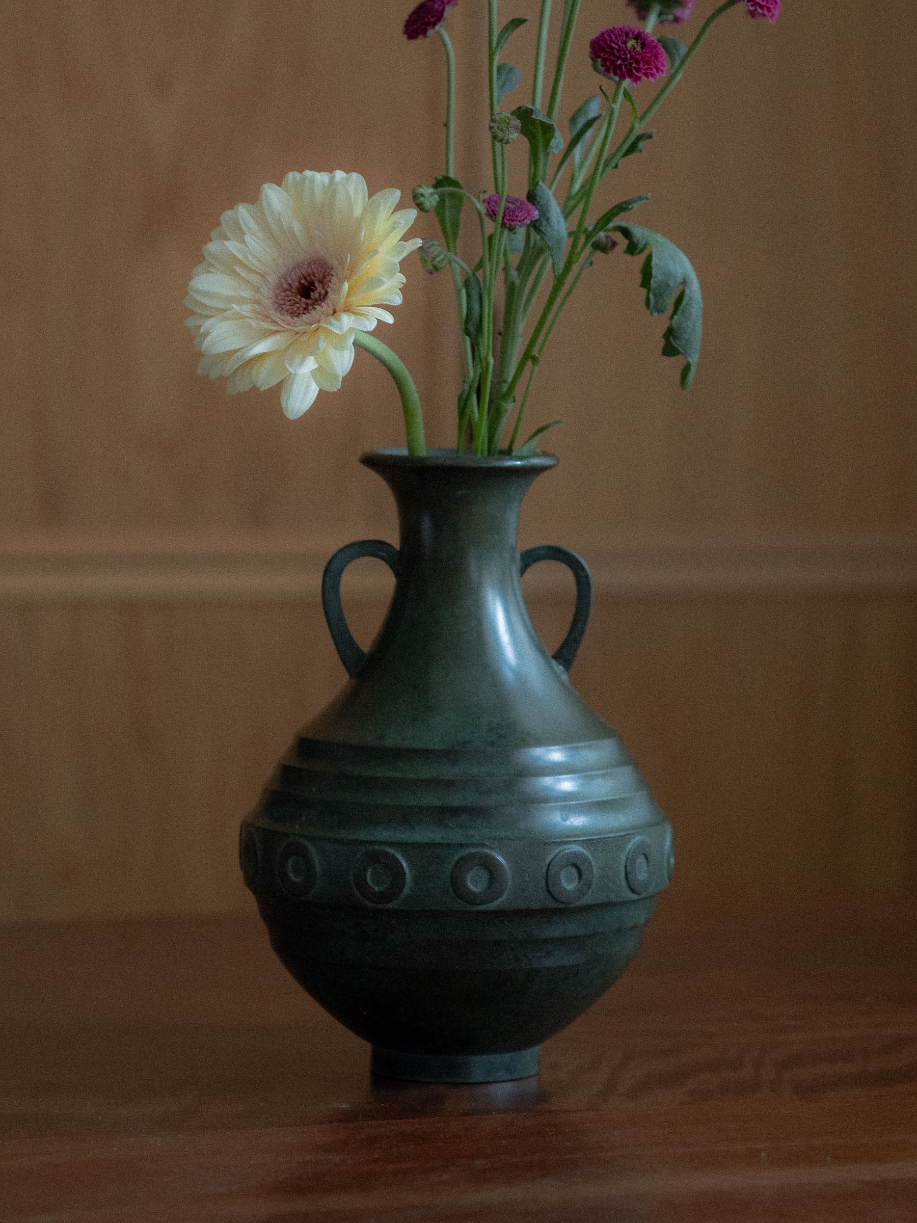 Murata Yoshio Janome bronze vase, Japan, Shōwa period, photographed with fresh flowers on a wooden table against warm wood panelling.