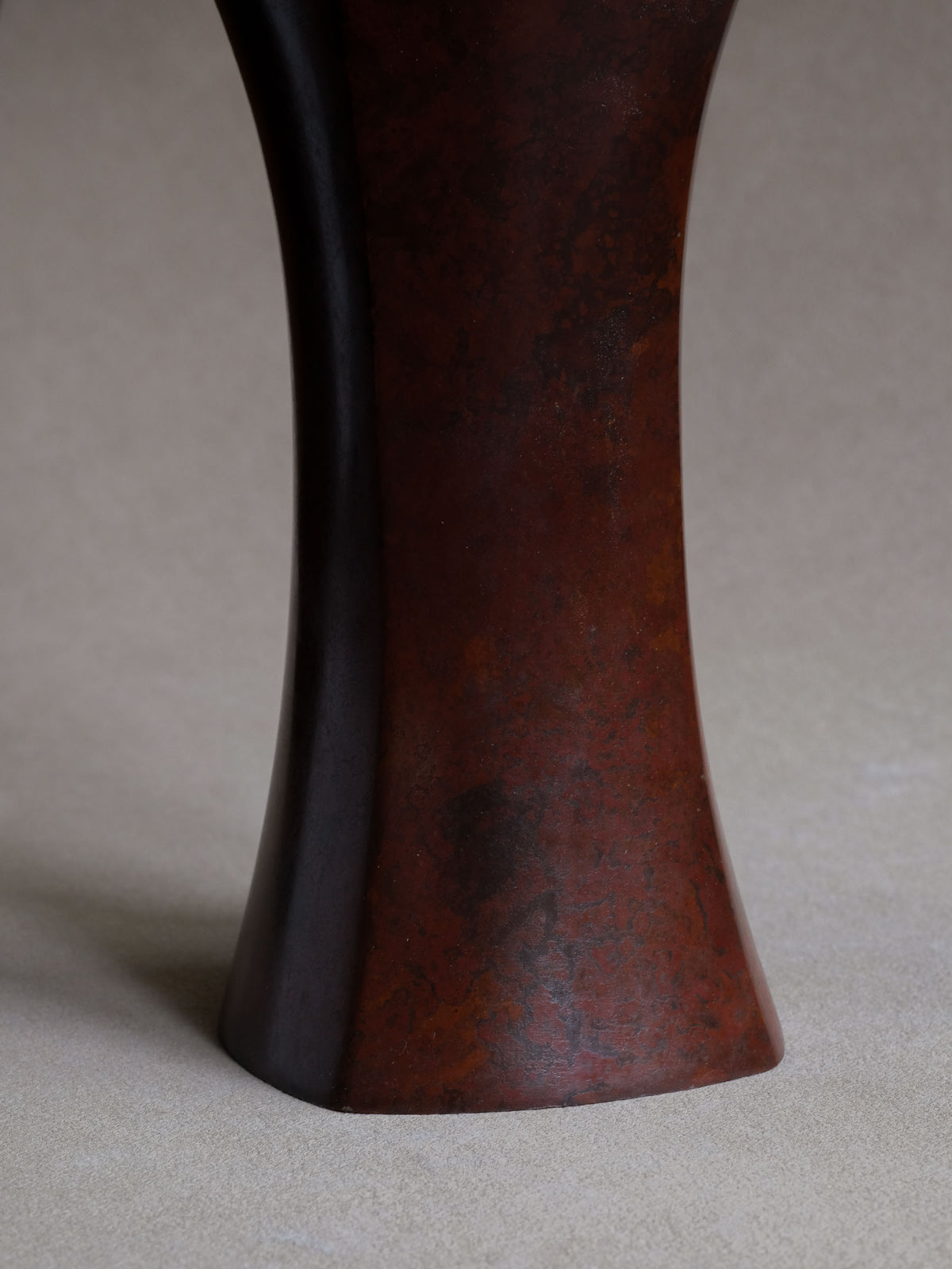Detail of the vase body showing its mottled purple-red bronze surface and gently widening base.