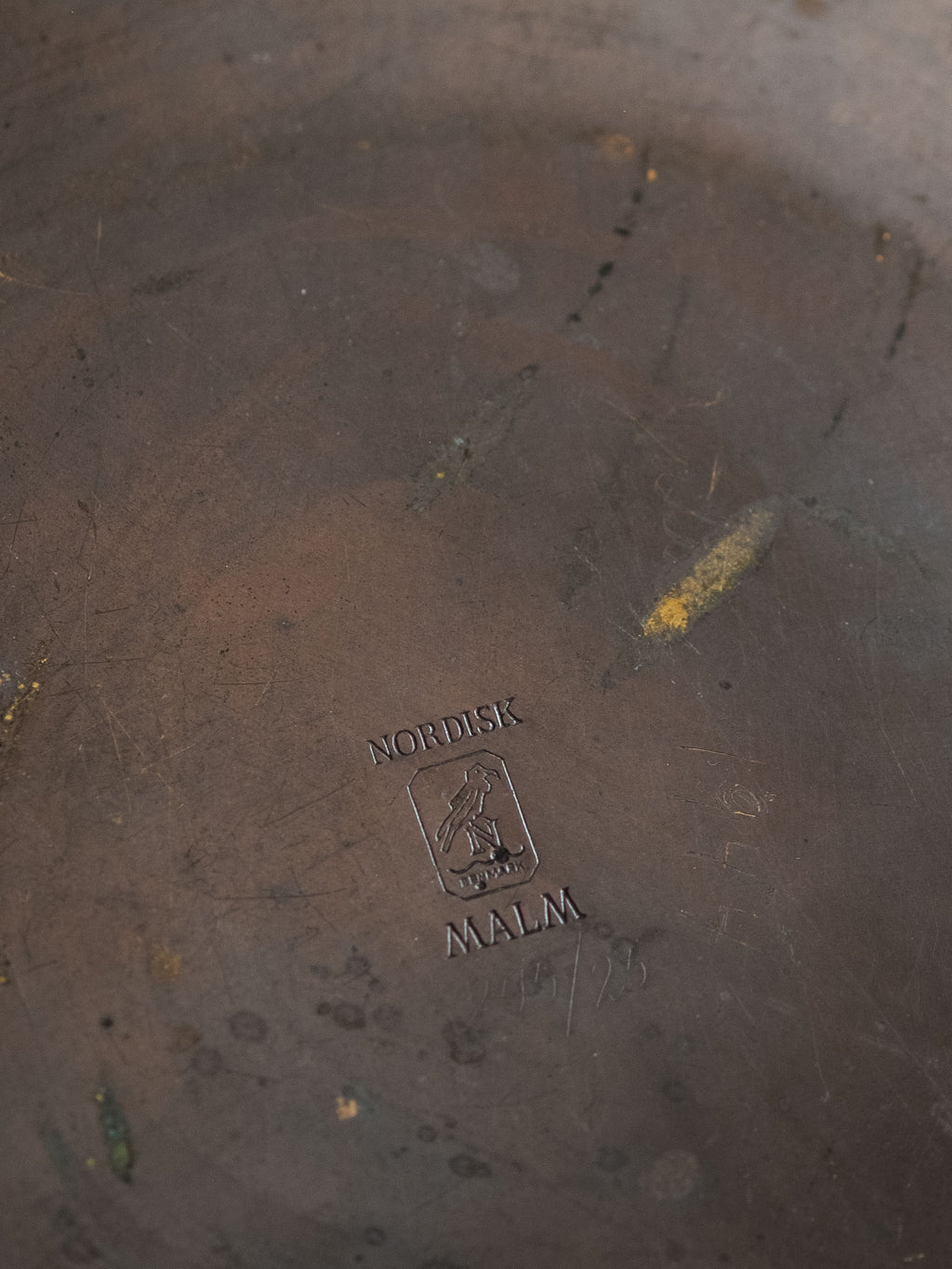 Close-up of the underside of the bronze dish showing the stamped Nordisk Malm maker’s mark and surface wear consistent with age.