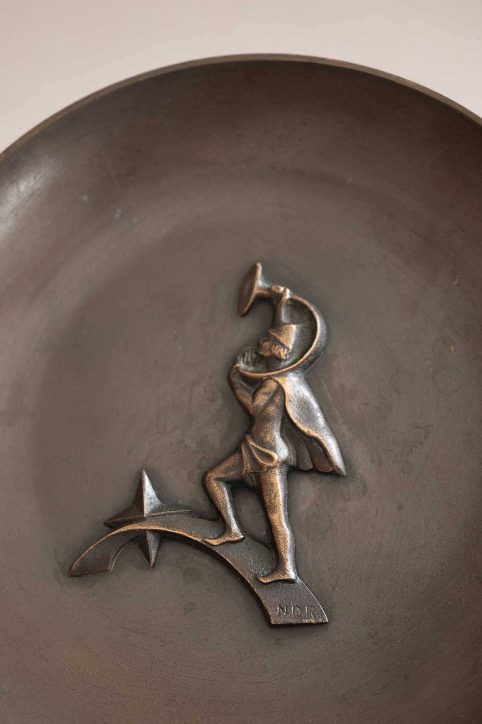 Close-up of the raised horn-blower relief inside the Nordisk Malm bronze dish, showing the dark patinated surface and NDR initials.