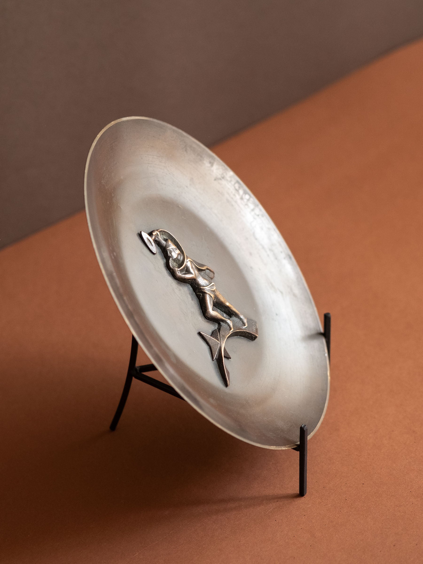 Decorative plate with a figurine on a stand against a brown background