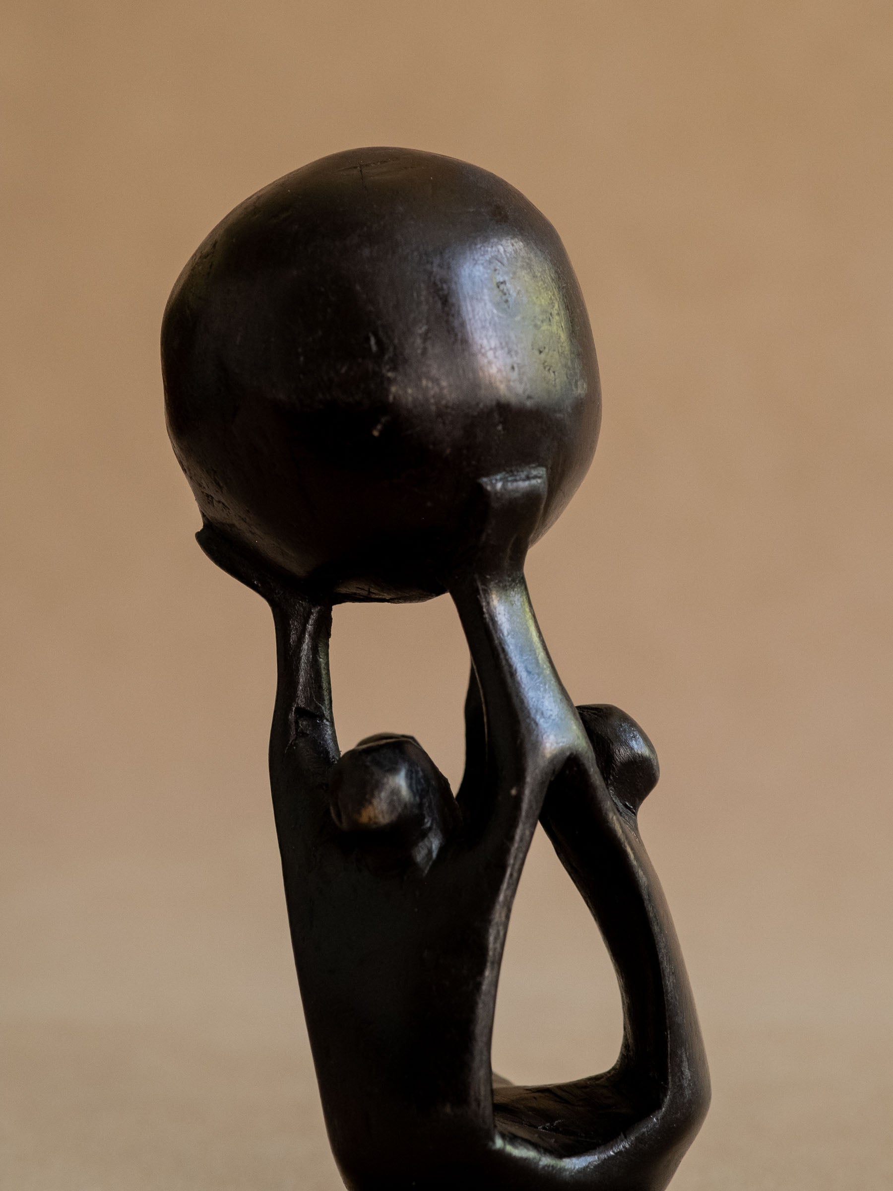 Three-quarter close view of the ebony three-figure sculpture, showing the raised sphere and carved negative spaces.