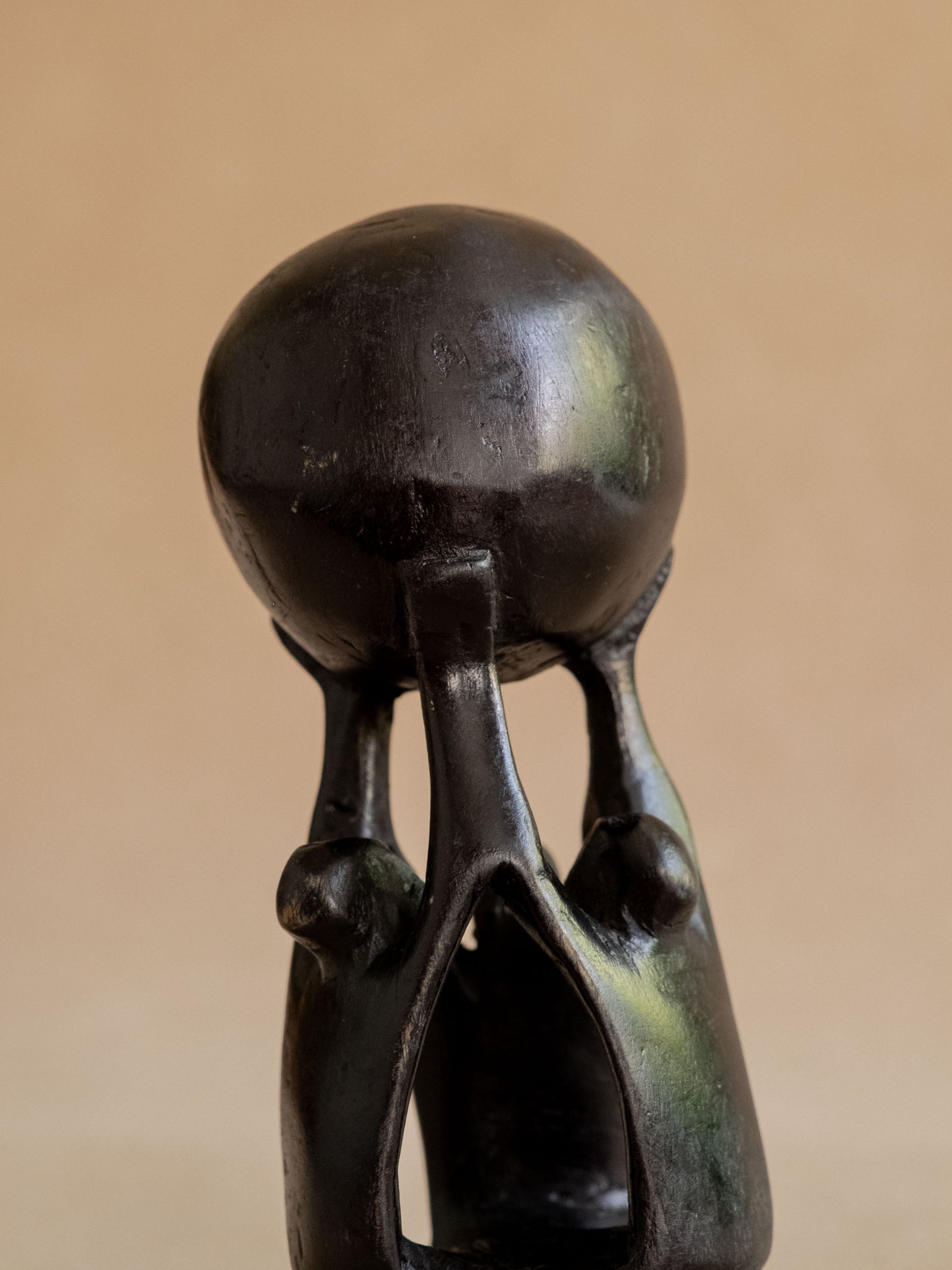Front close view of the Makonde-attributed ebony sculpture with three figures grouped beneath the sphere.