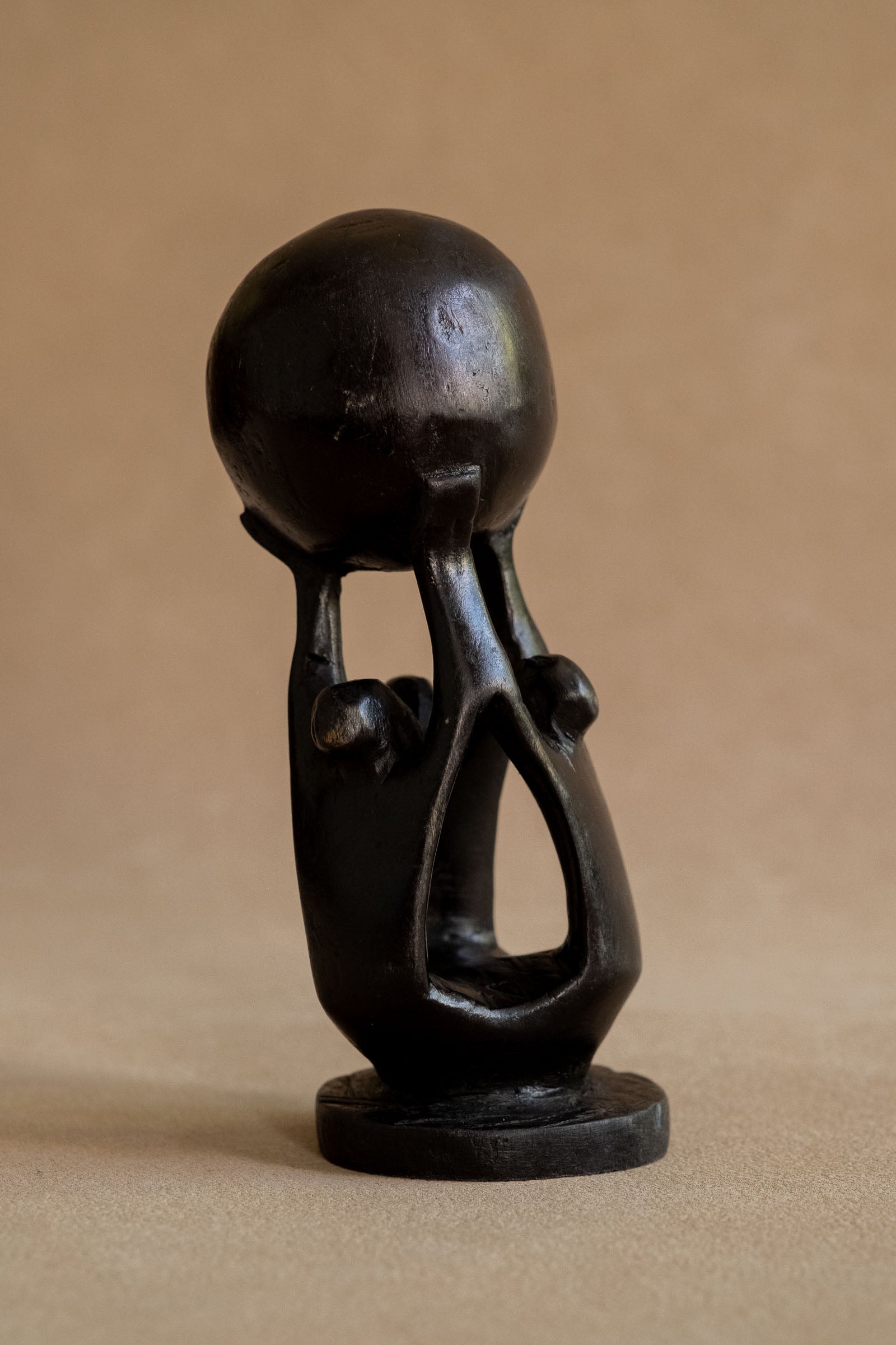 Full view of the compact ebony three-figure sculpture on its round base against a warm neutral background.