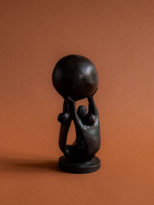 Hero view of the ebony Makonde-attributed sculpture from Tanzania against a reddish brown background.