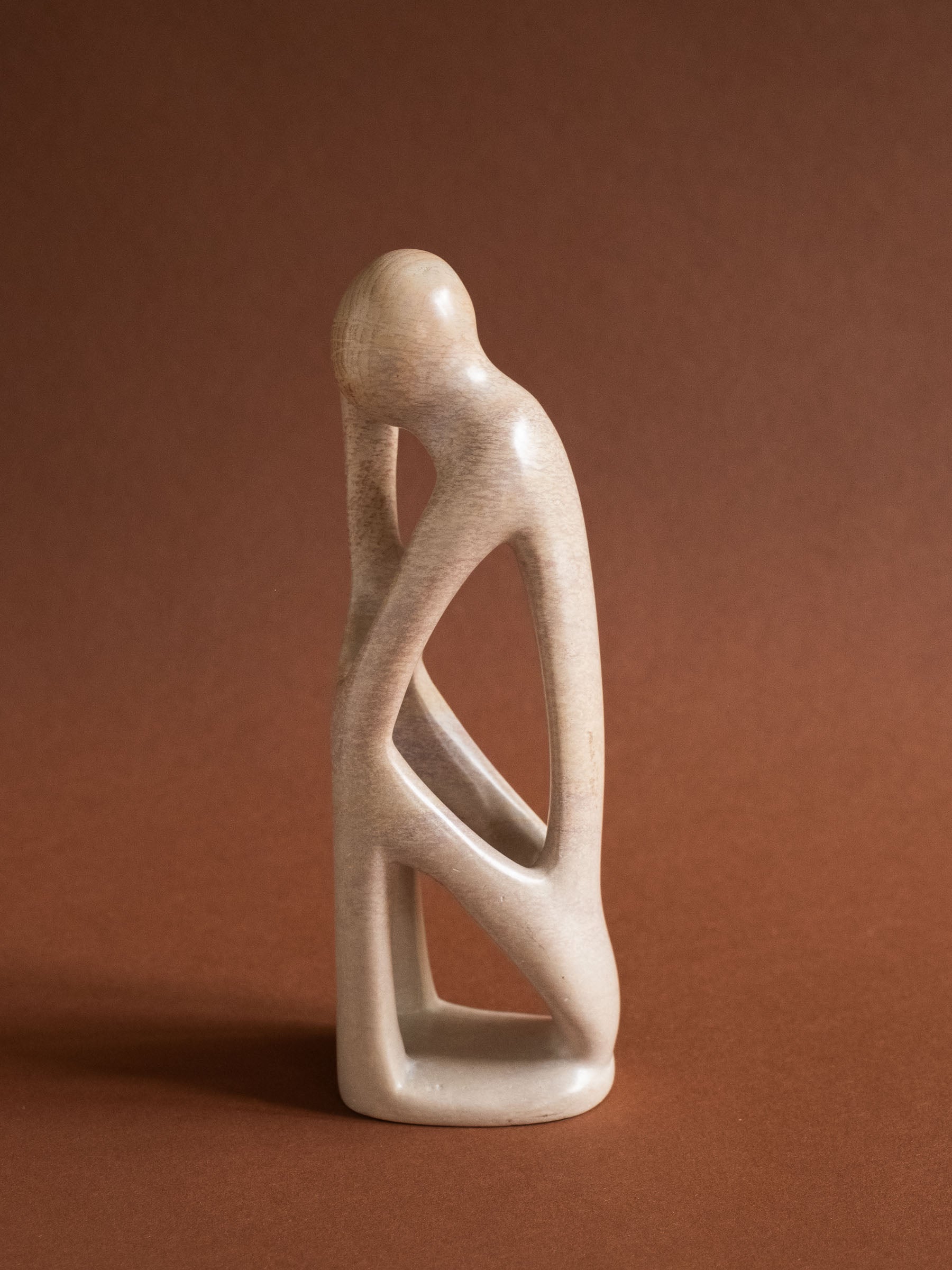 Full left-profile view of the abstract Kisii soapstone figure against a warm reddish background.