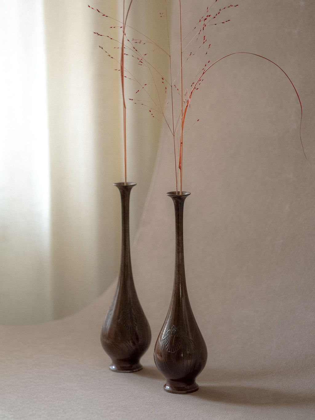 Pair of tall Japanese metal bud vases styled with dried grasses in an interior setting.