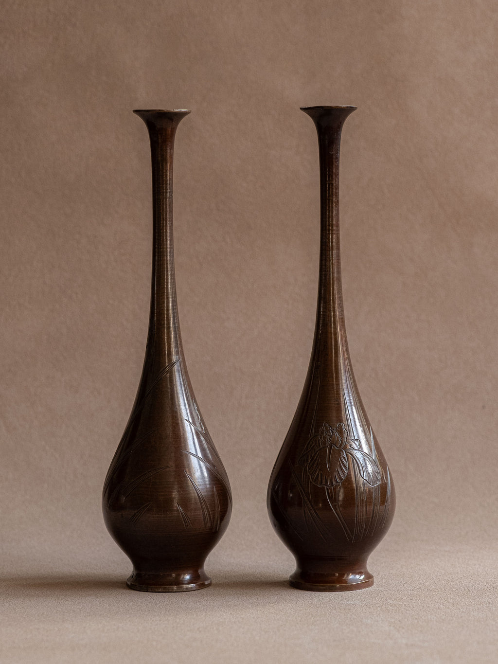 Pair of Japanese metal bud vases with brown patina and engraved iris and reed decoration, shown from the front.