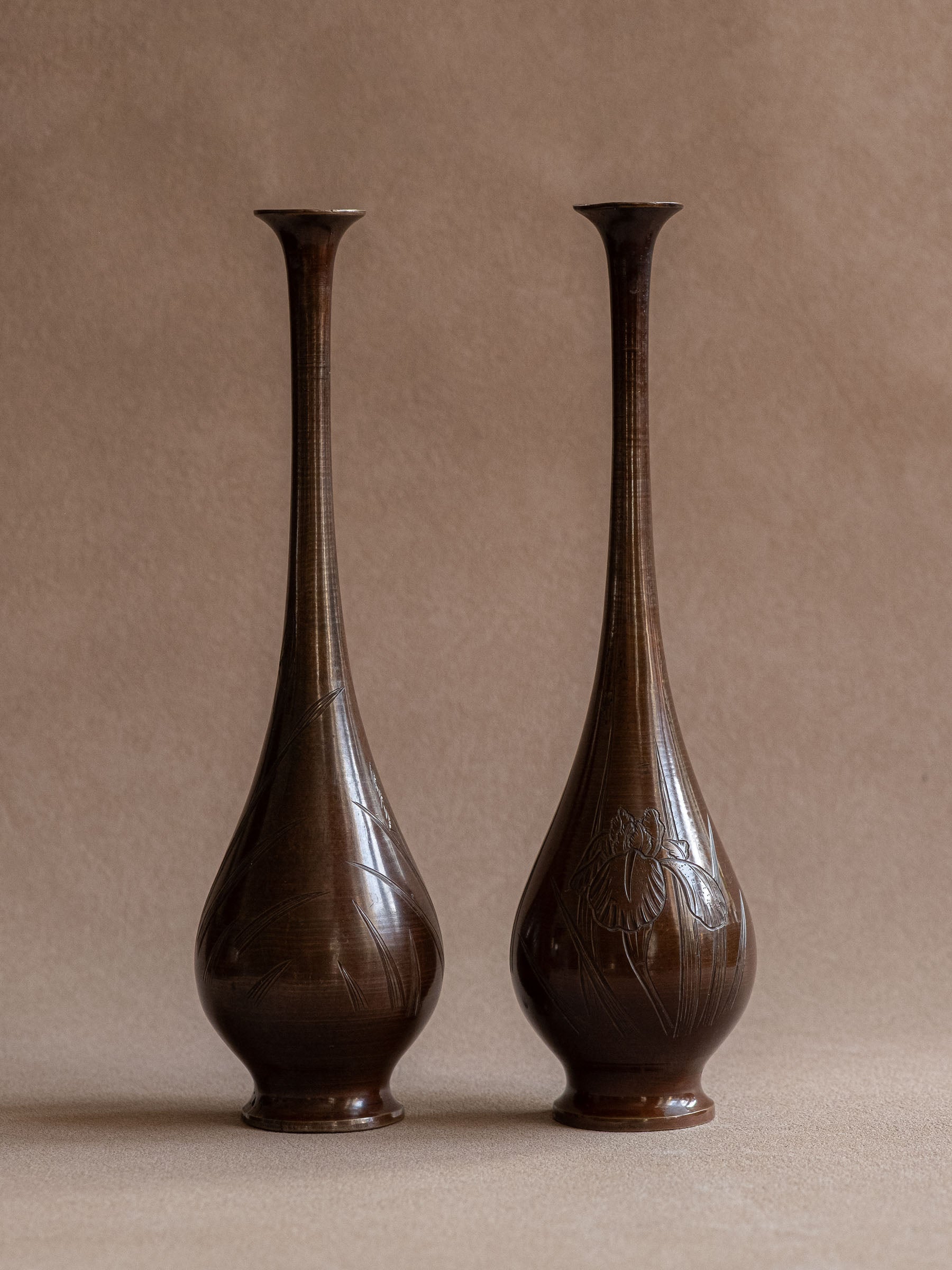 Pair of Japanese metal bud vases with brown patina and engraved iris and reed decoration, shown from the front.