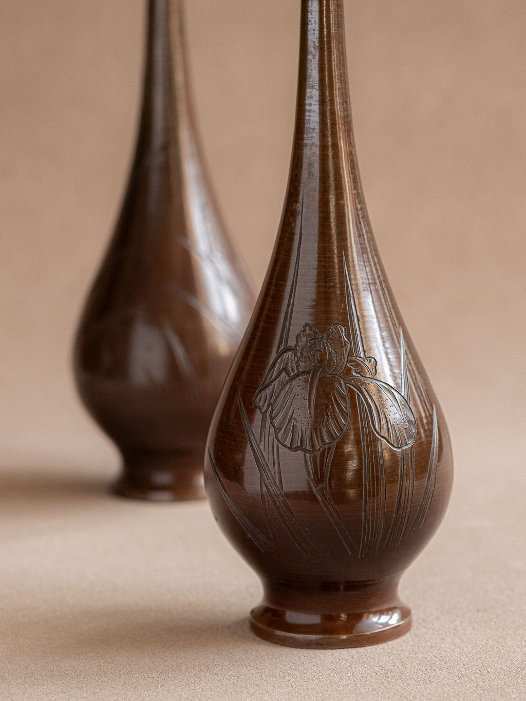 Close up of a pair of tall Japanese metal bud vases with long necks and rounded bodies.