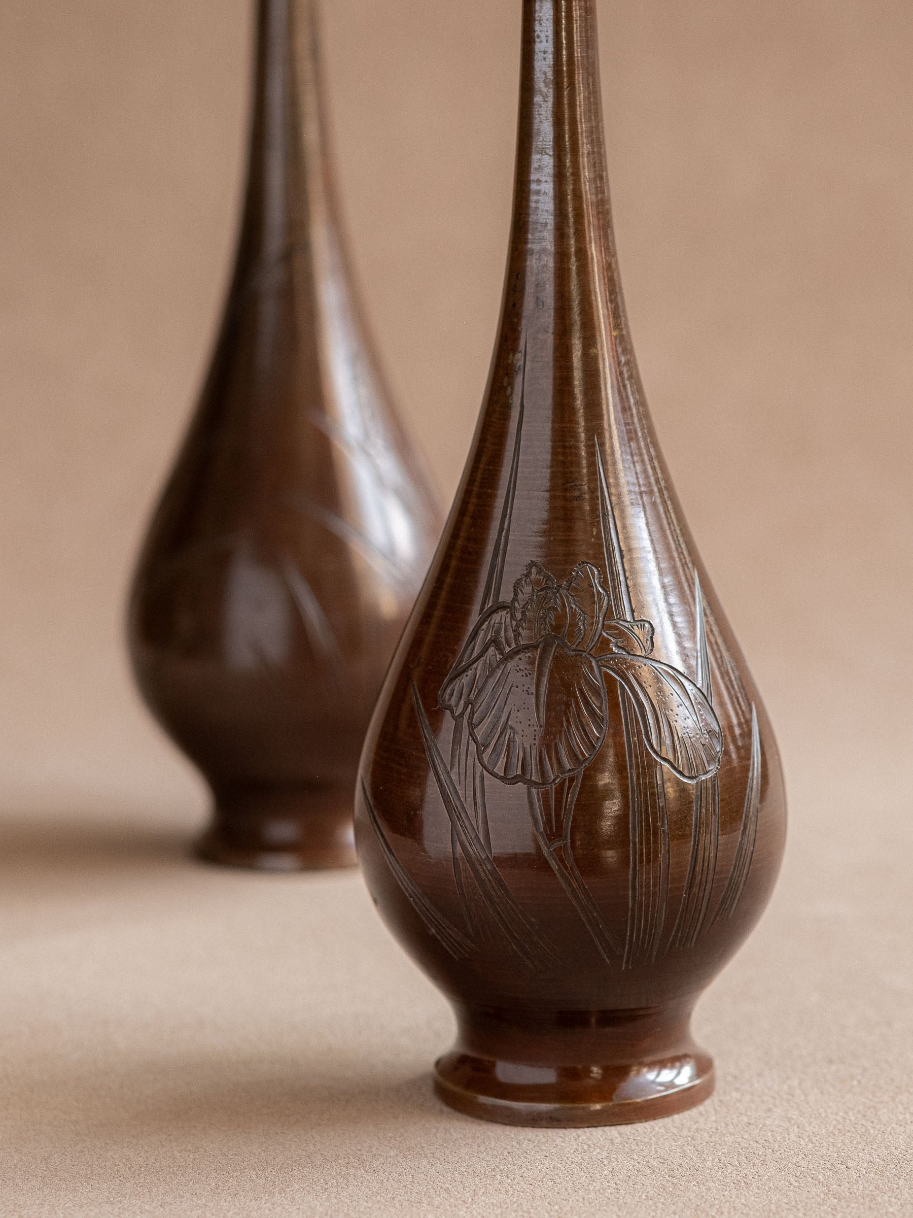 Close up of a pair of tall Japanese metal bud vases with long necks and rounded bodies.