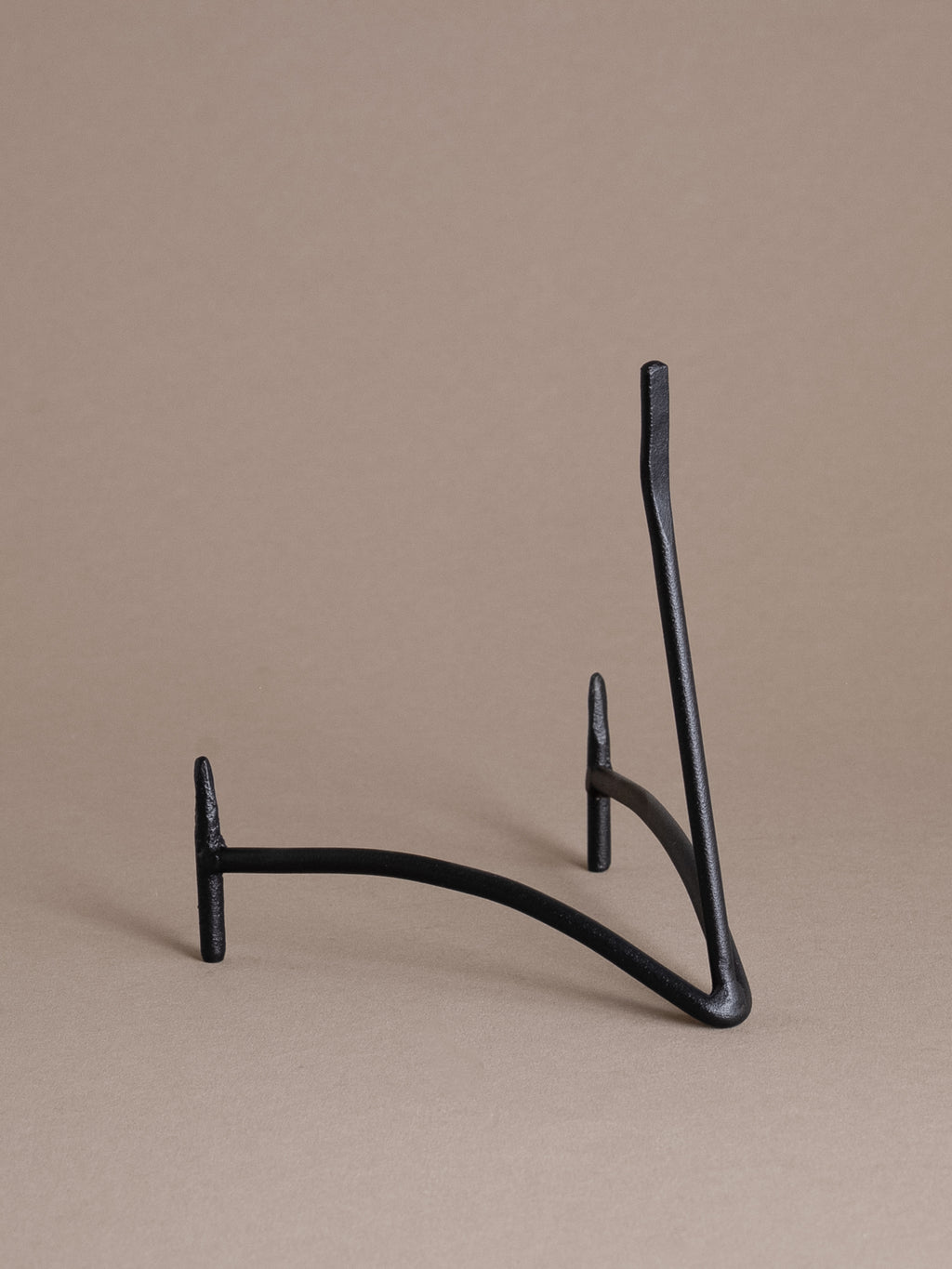 Side view of a black iron plate display stand with curved support and matte finish against a taupe background
