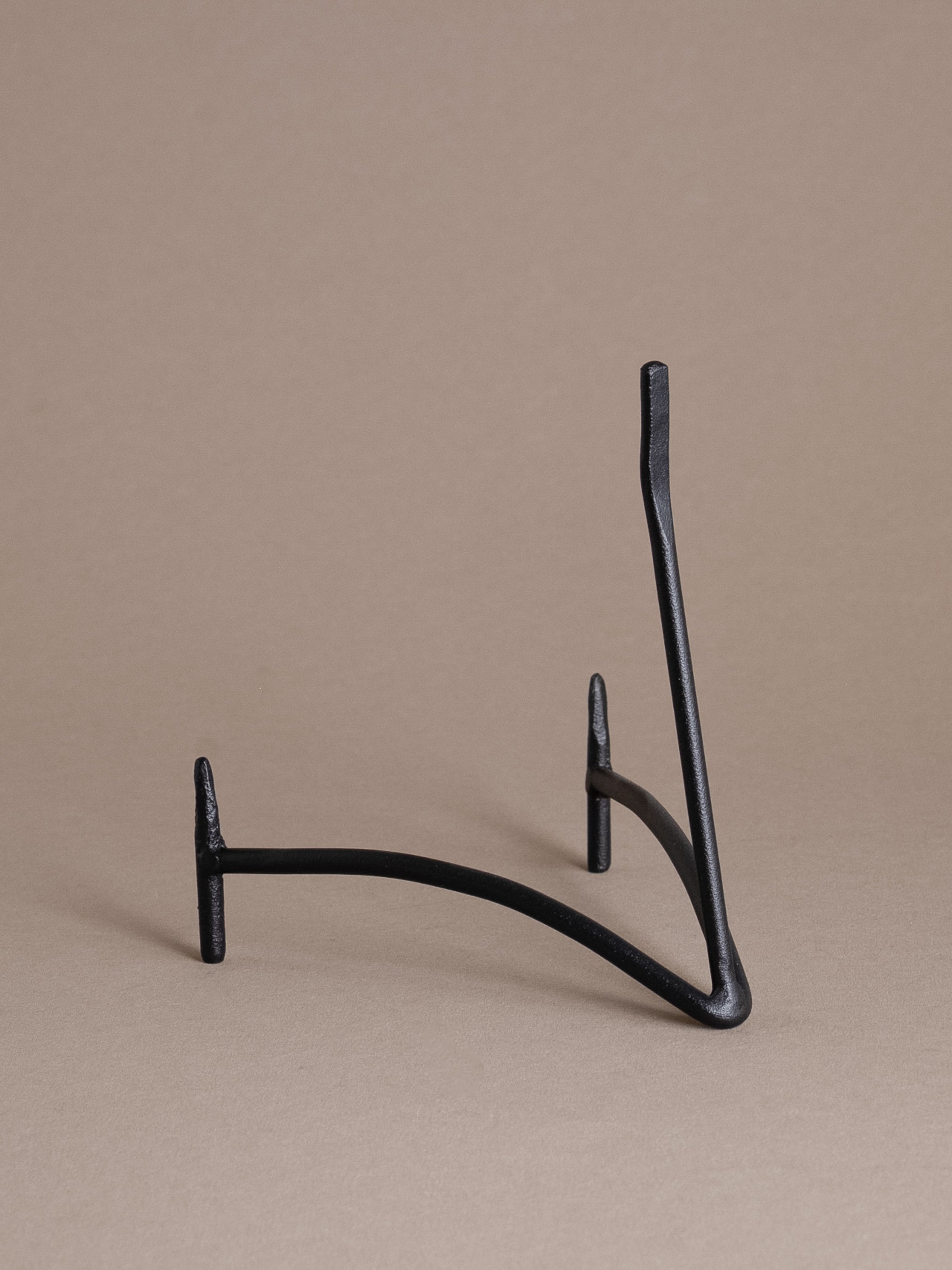 Side view of a black iron plate display stand with curved support and matte finish against a taupe background