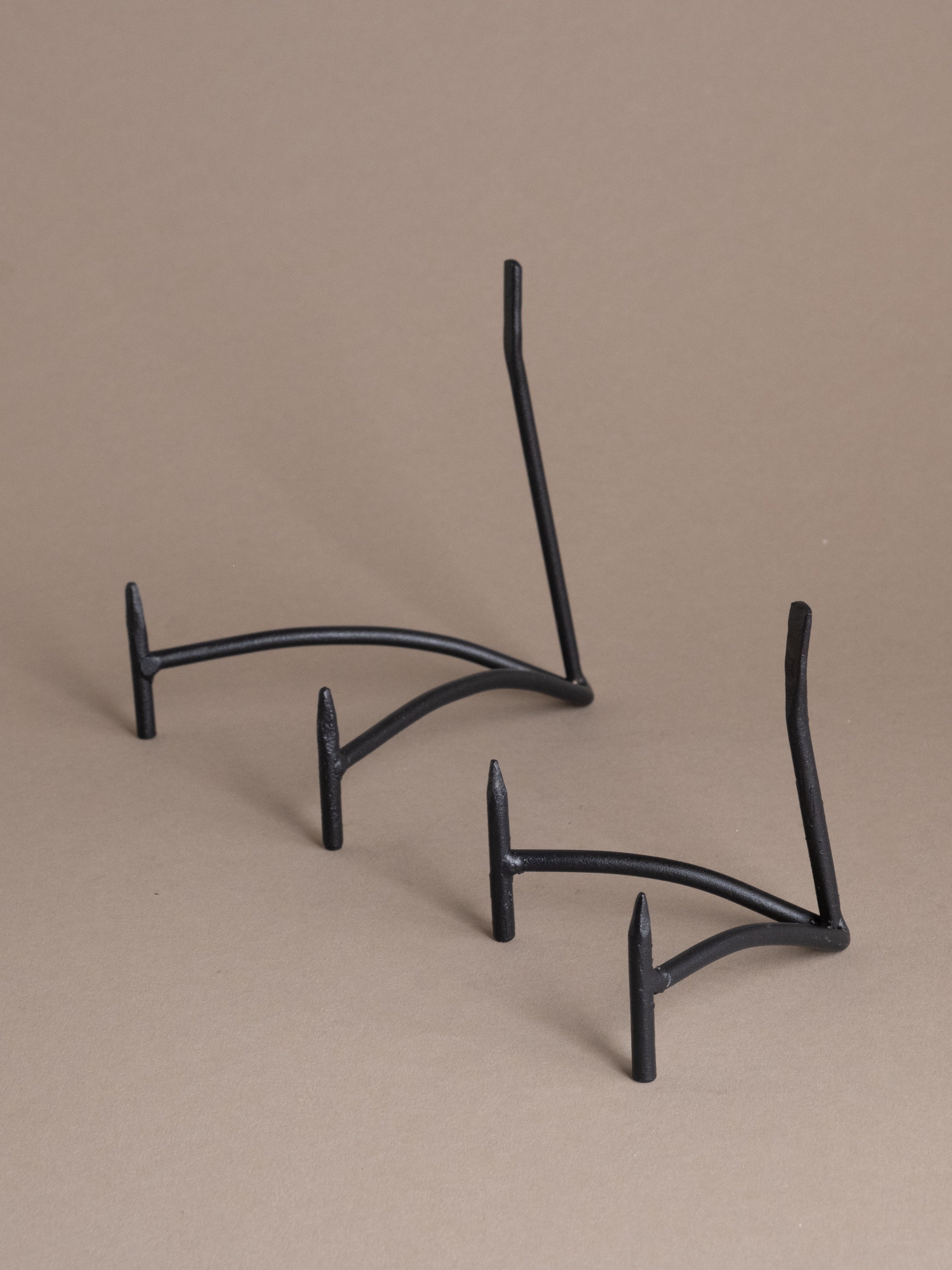 Two black iron plate display stands shown together against a taupe background, available in multiple sizes for plate and bowl display