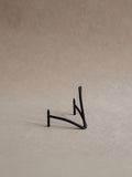 Small black iron plate stand shown empty against a warm beige background, with curved supports and a slim upright back