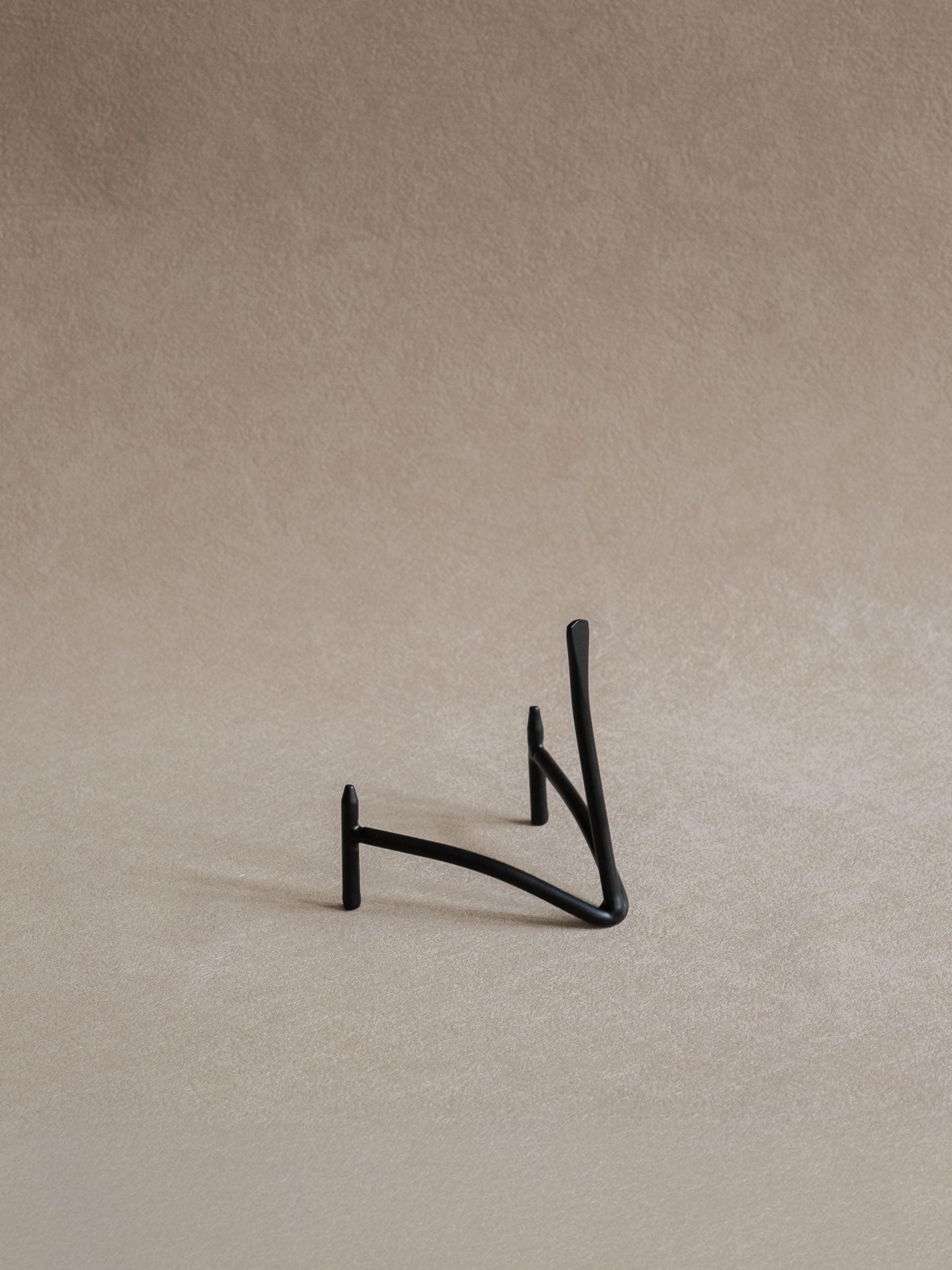 Small black iron plate stand shown empty against a warm beige background, with curved supports and a slim upright back