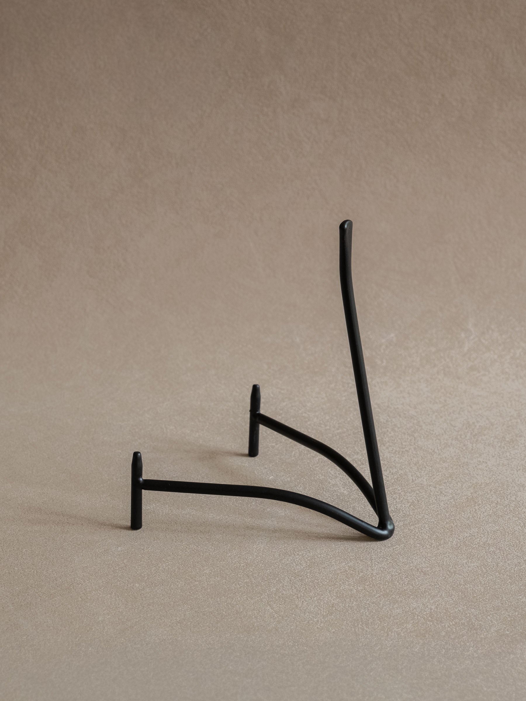 Side view of a black iron plate stand with curved base, front supports, and tall upright back against a warm beige background