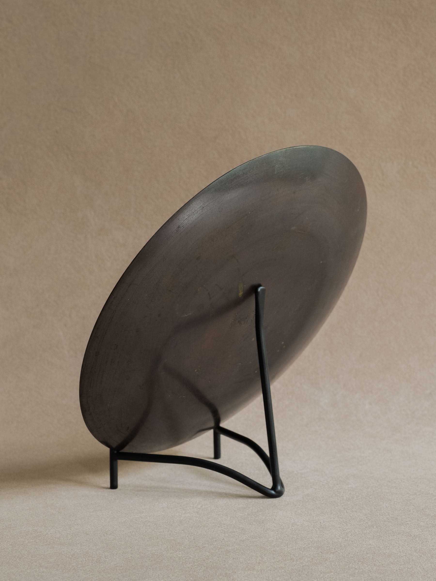 Black iron plate stand holding a dark metal plate at a slight angle against a warm beige background