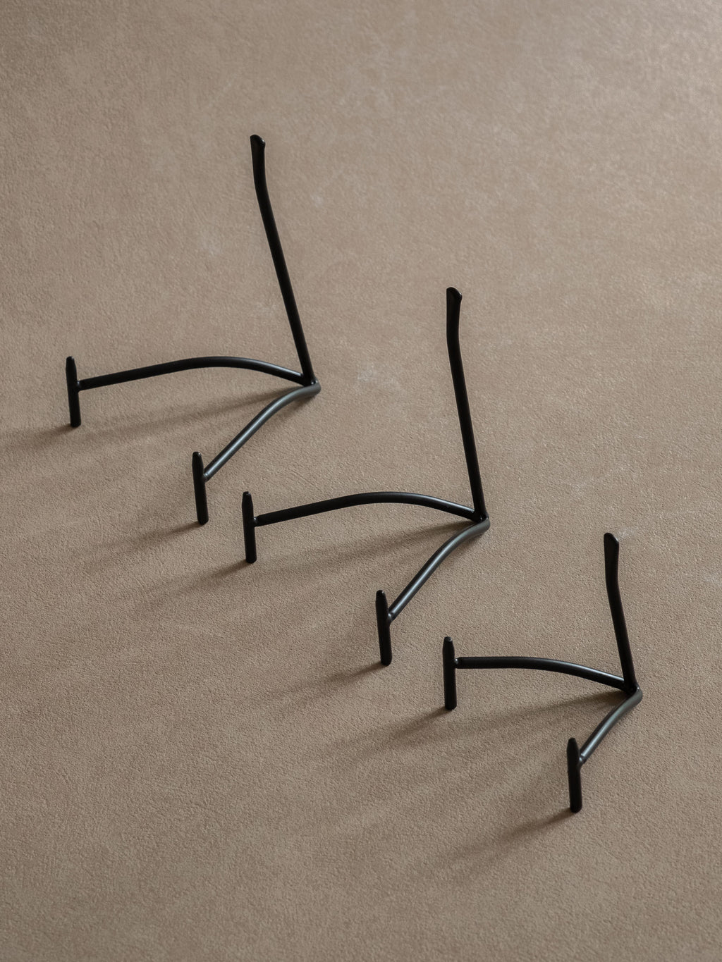Three black iron plate stands in small, medium, and large sizes arranged diagonally against a warm beige background