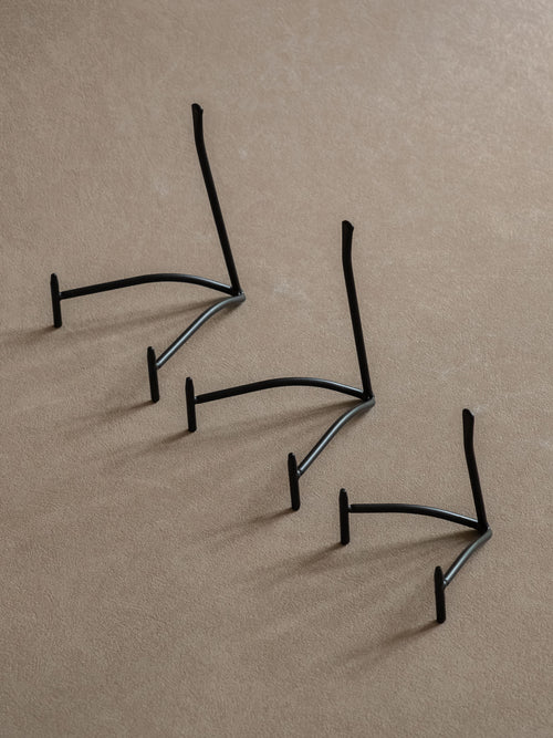 Three black iron plate stands in small, medium, and large sizes arranged diagonally against a warm beige background