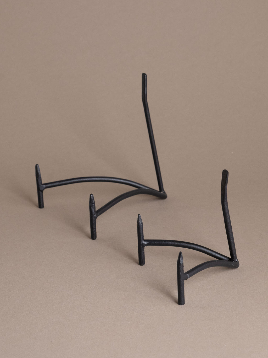 Two black iron plate display stands with curved support and matte finish against a taupe background
